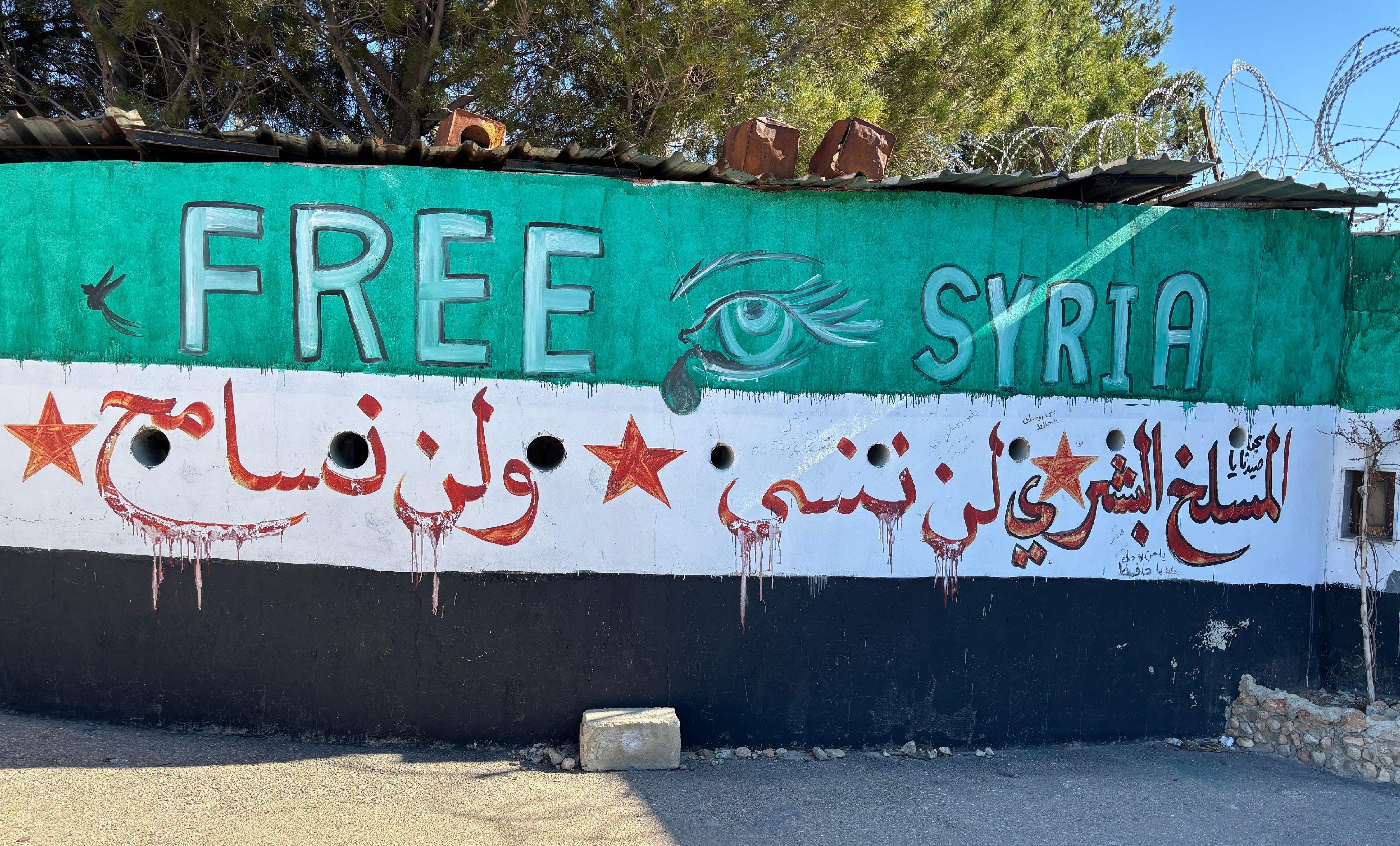 حائط مرسوم عليه علم سوريا الجديد ومرفق بعبارة تتحدث عن سجن صيدنايا: "المسلخ البشري لن ننسى ولن نسامح".