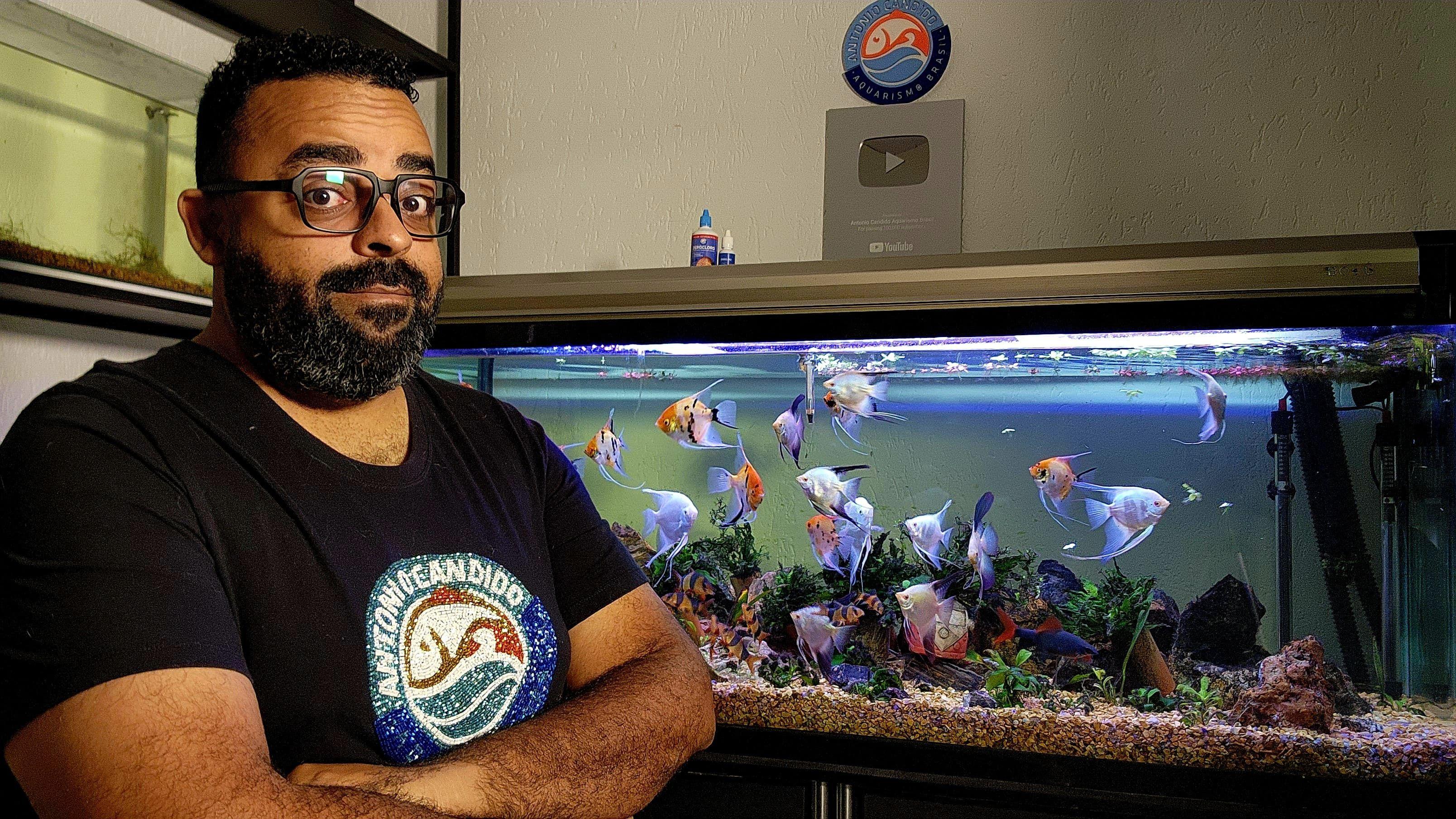 Aquarista Antonio Candido com um aquário atrás e peixes coloridos