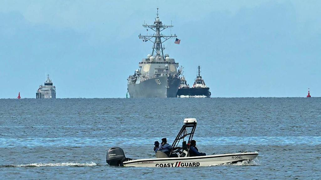 El destructor USS Gravely se observa al fondo de la imagen en la costas de Trinidad y Tobago. Más cerca, hay una lancha del servicio de Guardacostas de Trinidad y Tobago.