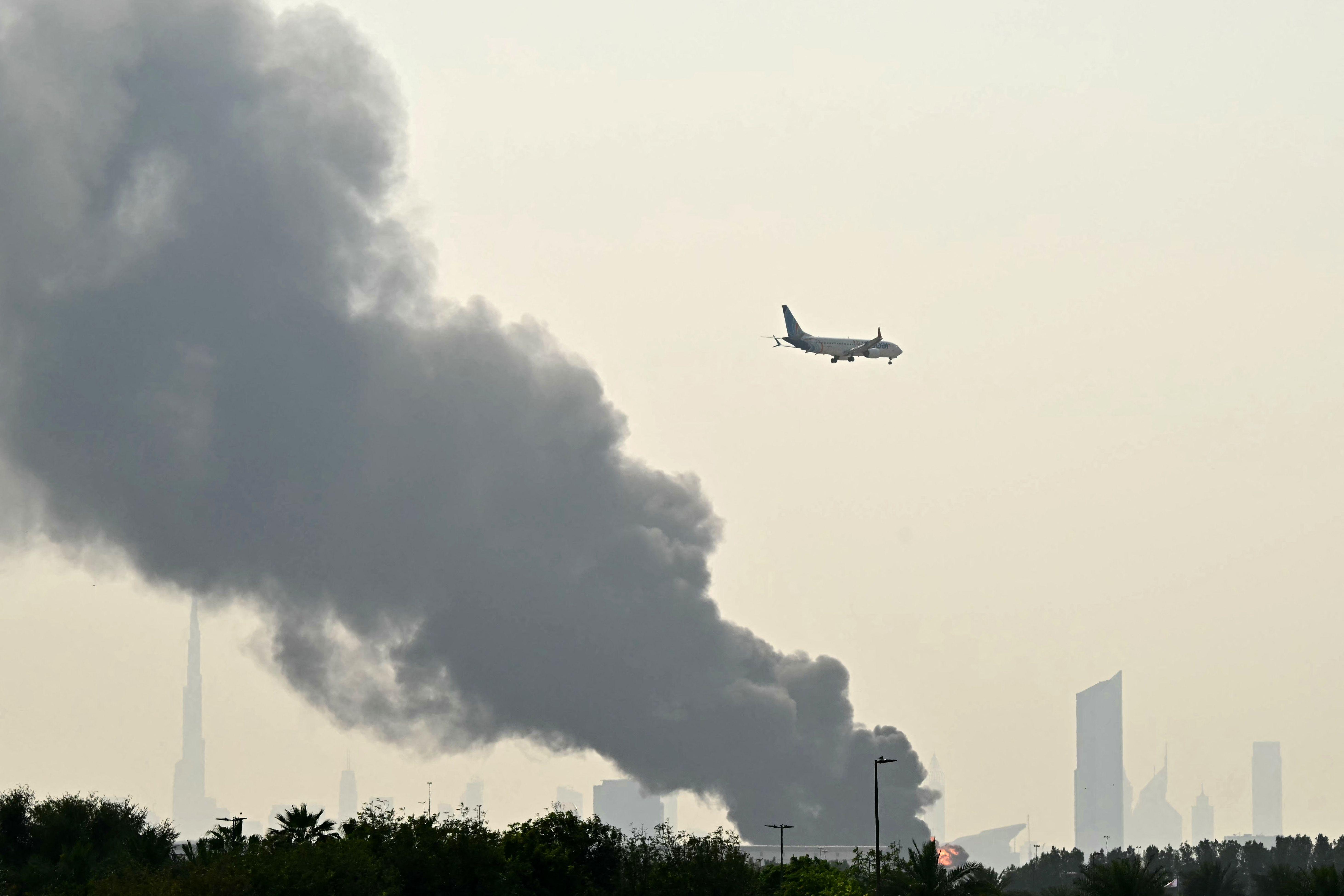 A plane is flying in the sky while plumes of smoke can be seen from an ongoing fire near Dubai International Airport