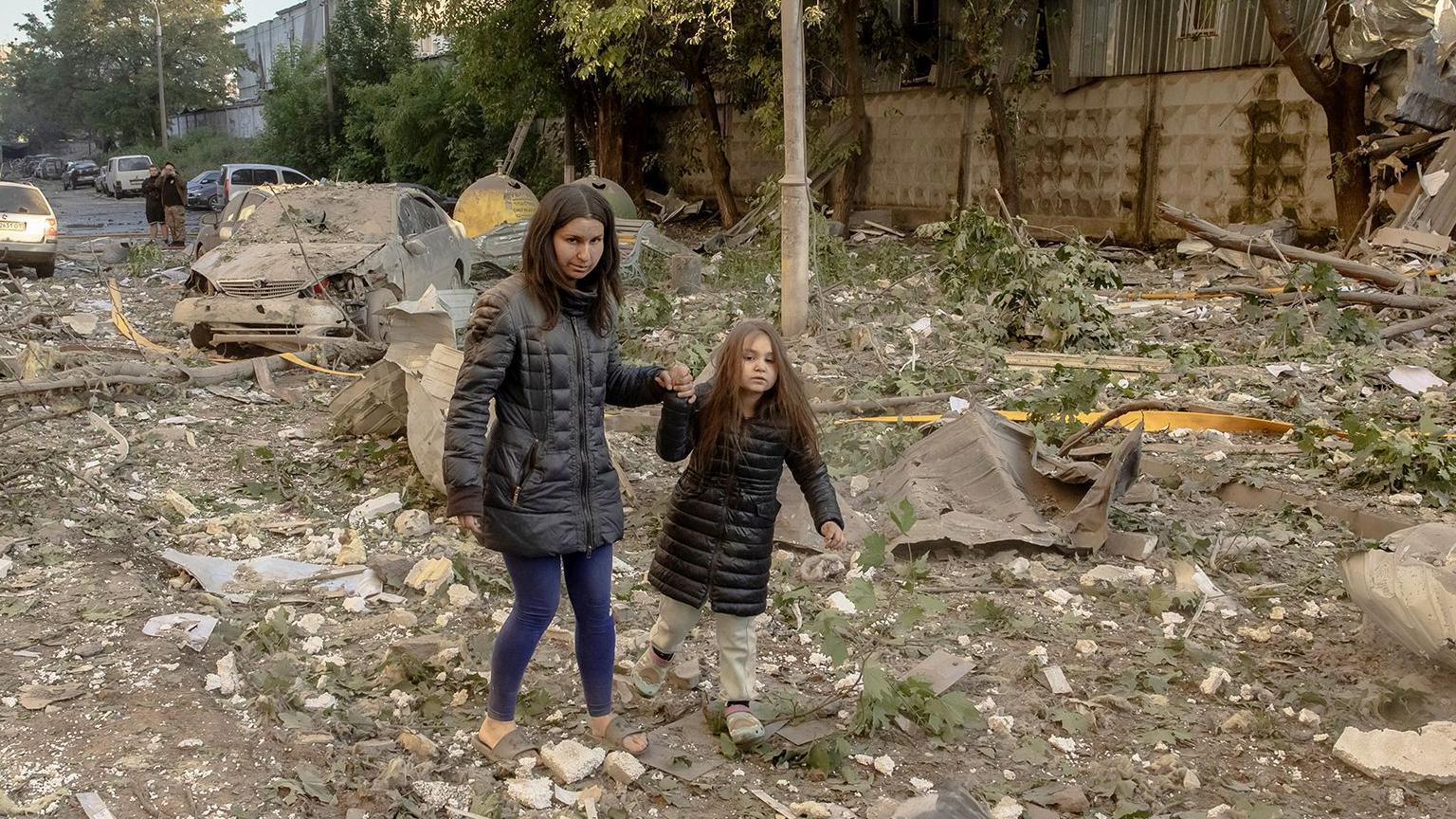 A primera hora de la mañana, una mujer y una niña pequeña caminan de la mano sobre una zona de escombros y escombros en Kiev.