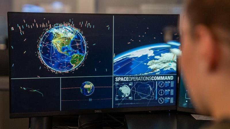 Soldado olha para tela de computador mostrando o planeta Terra e objetos em sua órbita.