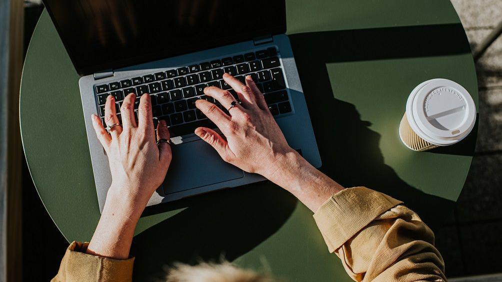 Čovek sedi na stolu i kuca na laptopu