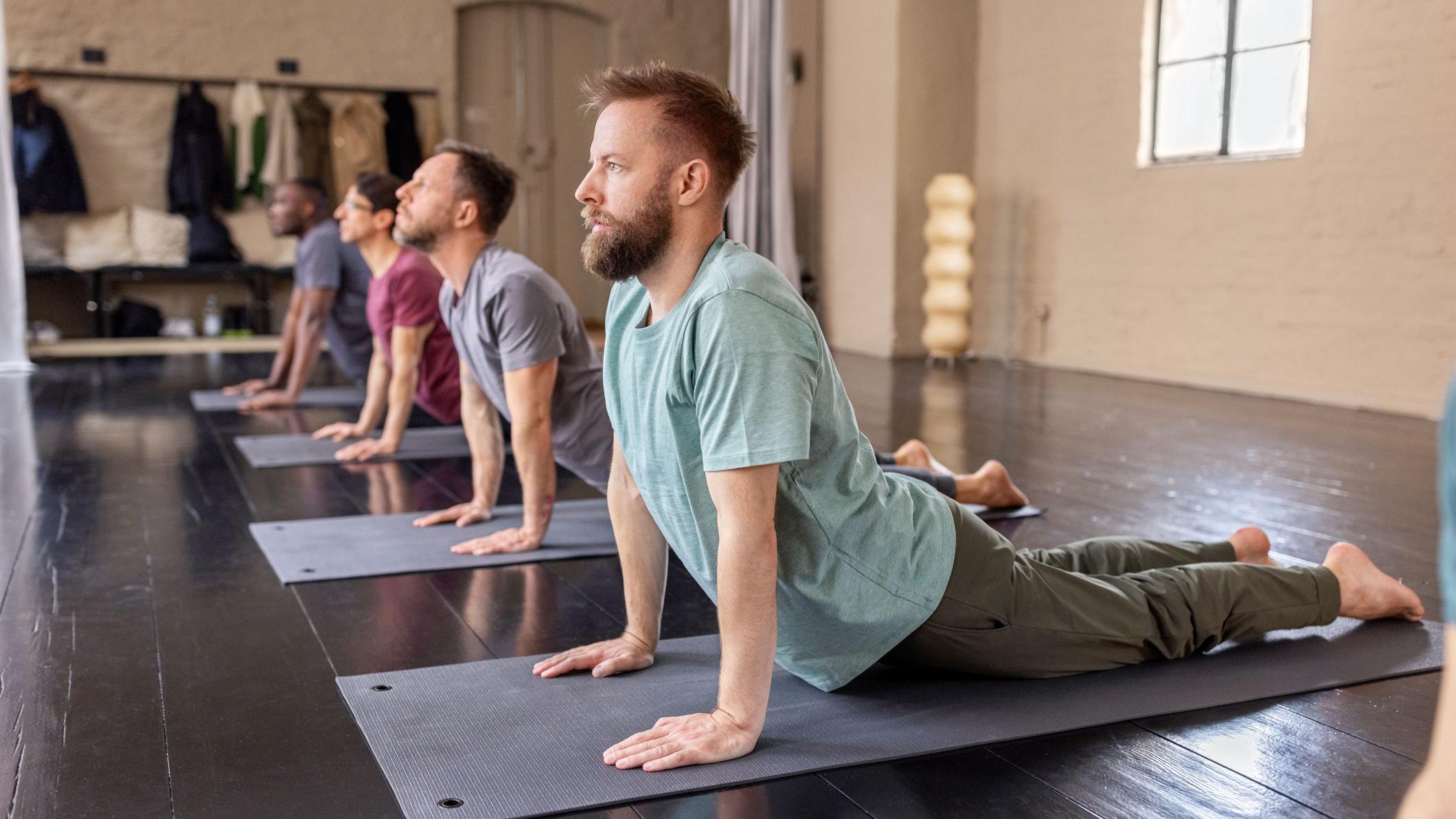Grupo diverso de hombres practicando la postura de la cobra en una clase de yoga.