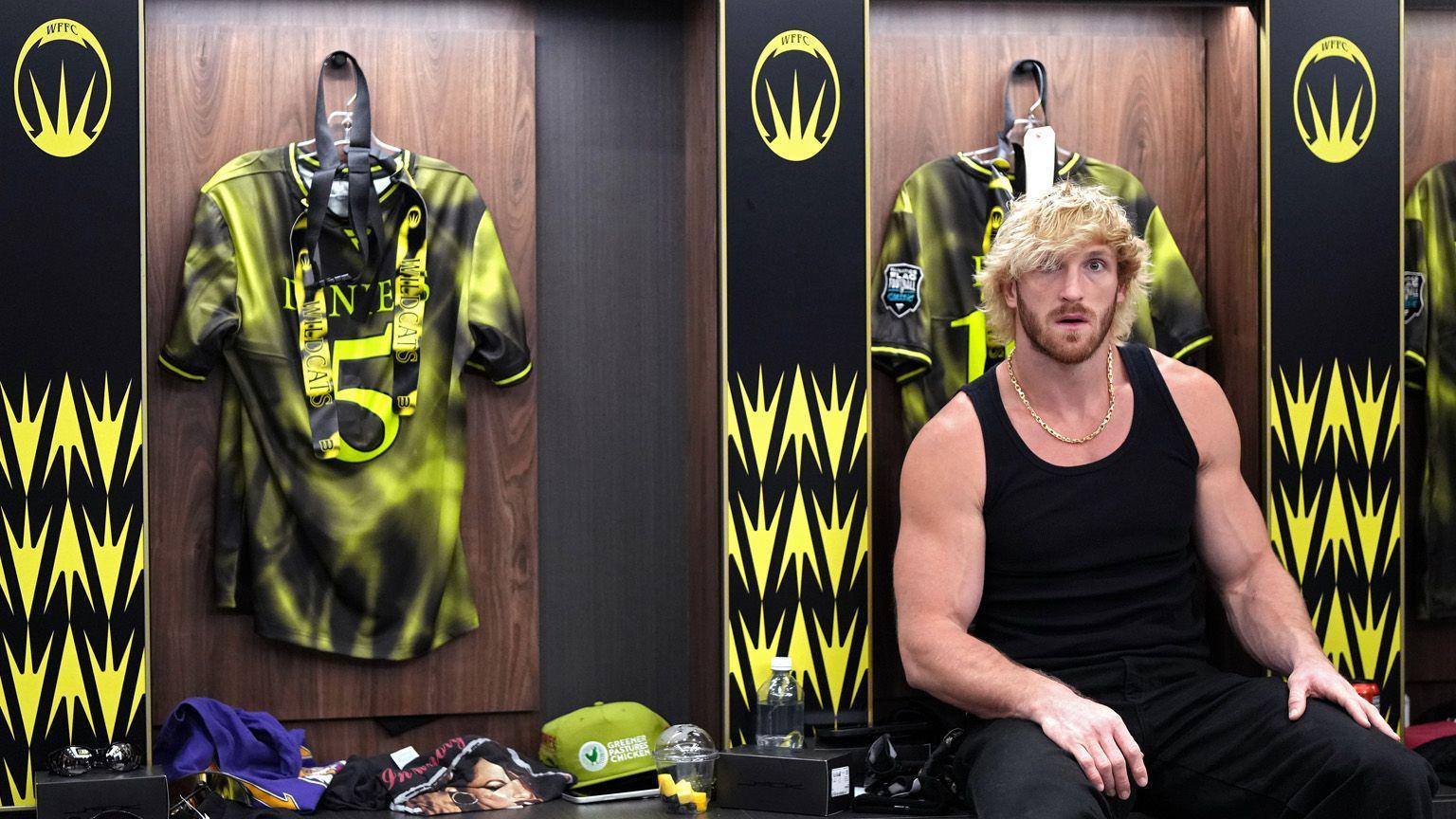 Logan Paul, homem musculoso de cabelo loiro platinado, veste uma regata preta enquanto est&aacute; sentado em um vesti&aacute;rio