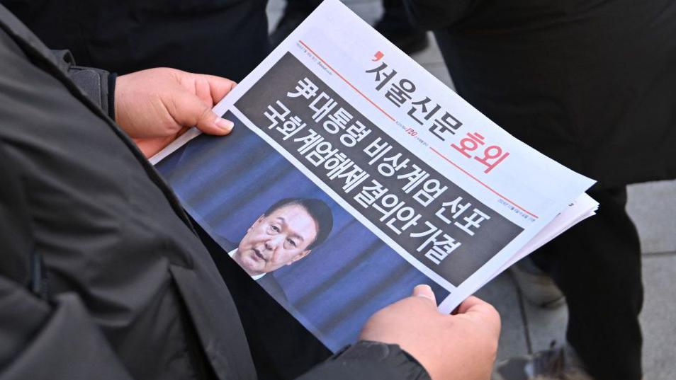 Um homem l&ecirc; uma edi&ccedil;&atilde;o extra de jornal no centro de Seul, com Yoon Suk-yeol na capa.