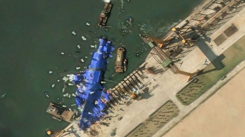 一張空拍衛星影像顯示，一艘停靠在港口的軍艦被藍色布料覆蓋，周圍環繞著數艘小型船隻