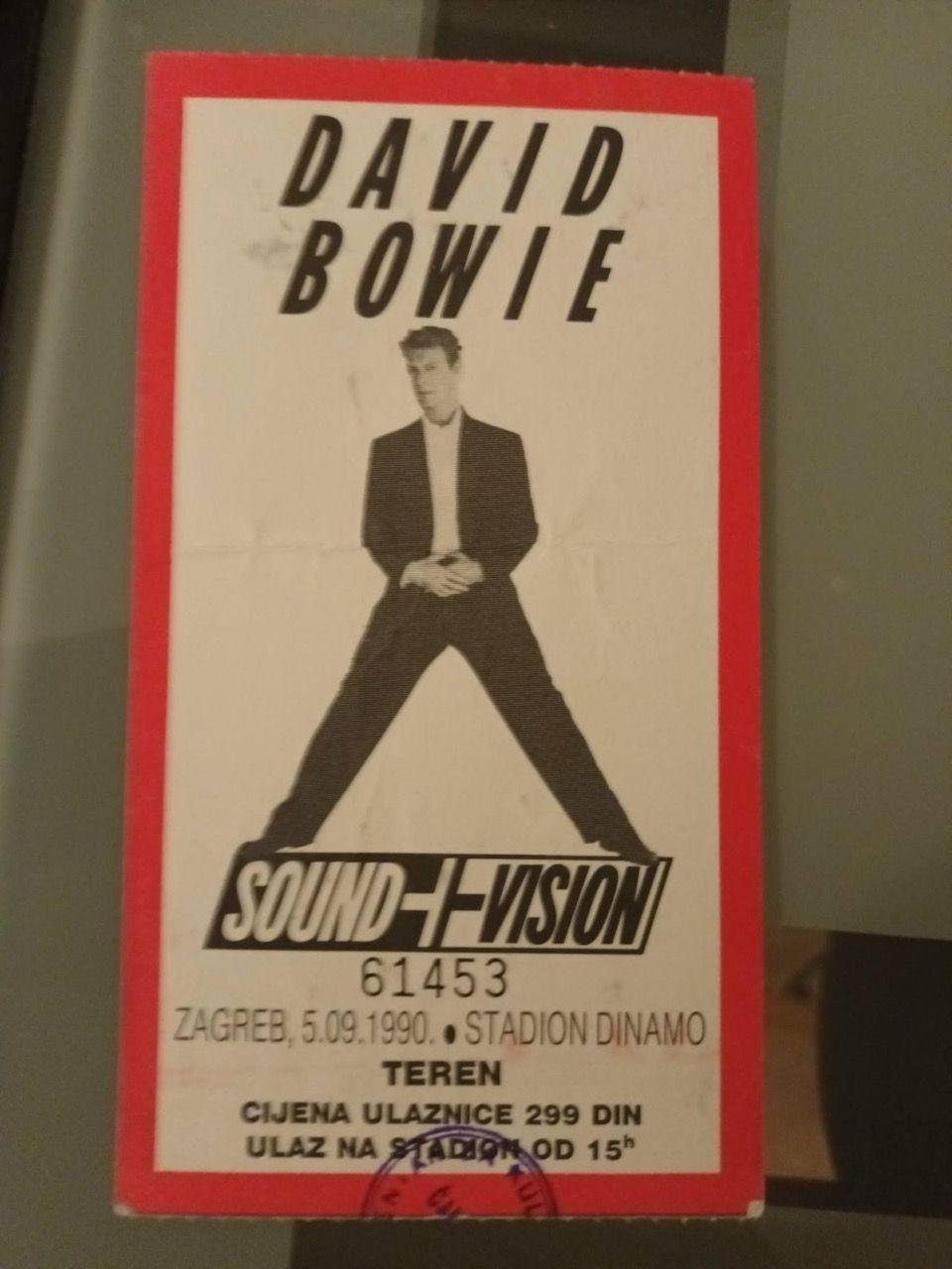 Koncertna ulaznica na kojoj je Dejvid Bouvi u crnim pantalonama i sakou, ispod kojeg ima belu košulju