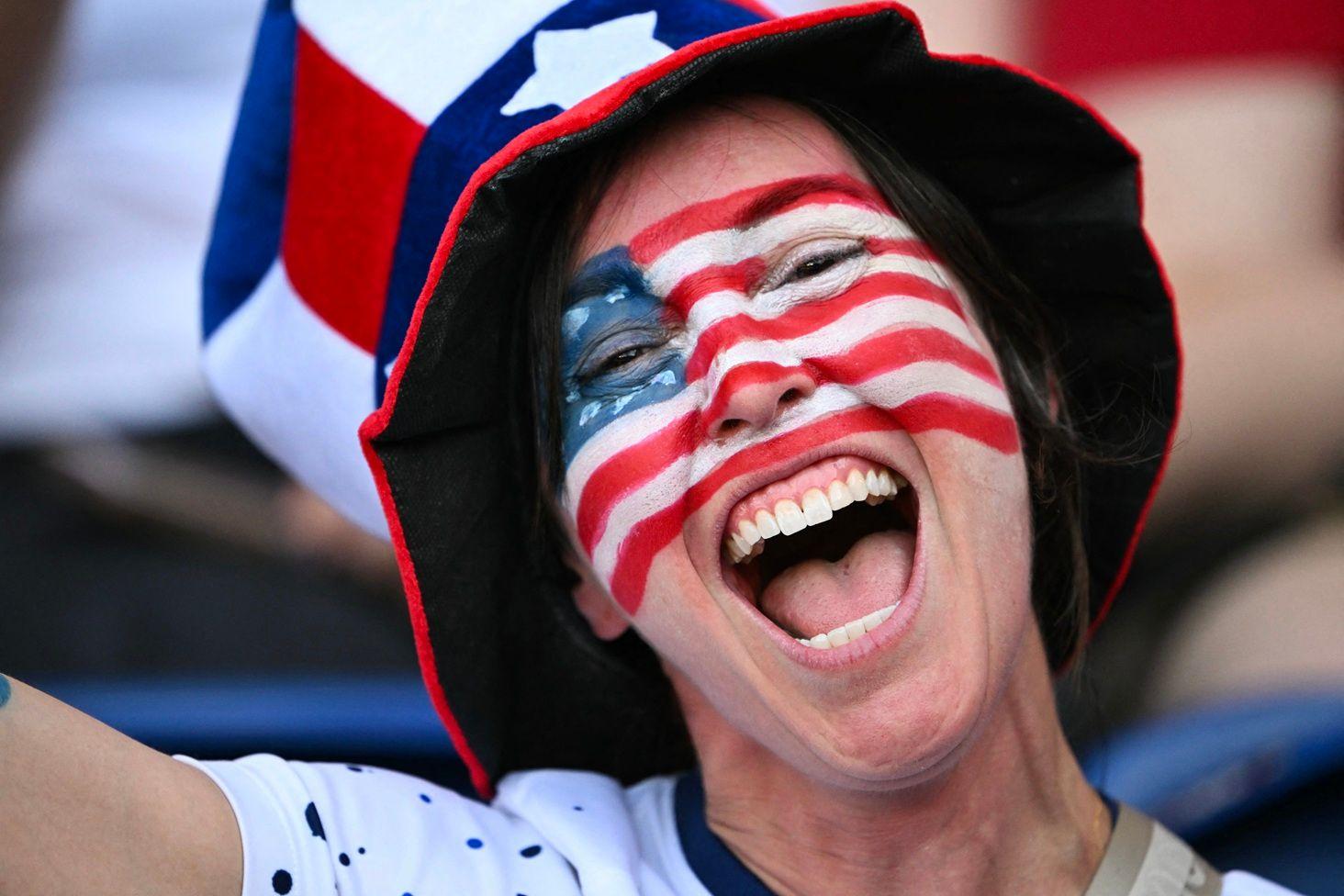 Una mujer sonriente con la bandera dibujada de EE.UU. dibujada en el rostro y con un sombrero y los colores de la bandera.
