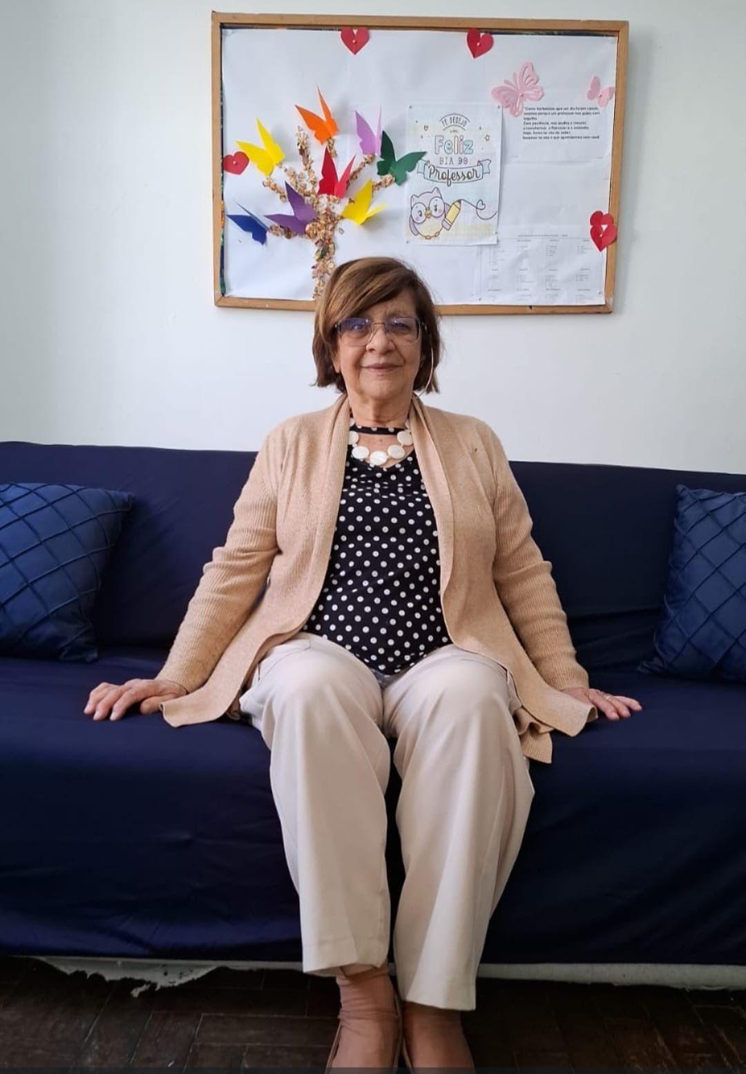 Retrato de corpo inteiro de Celi Ferreira, mulher de 82 anos, sentada no sof&aacute; 