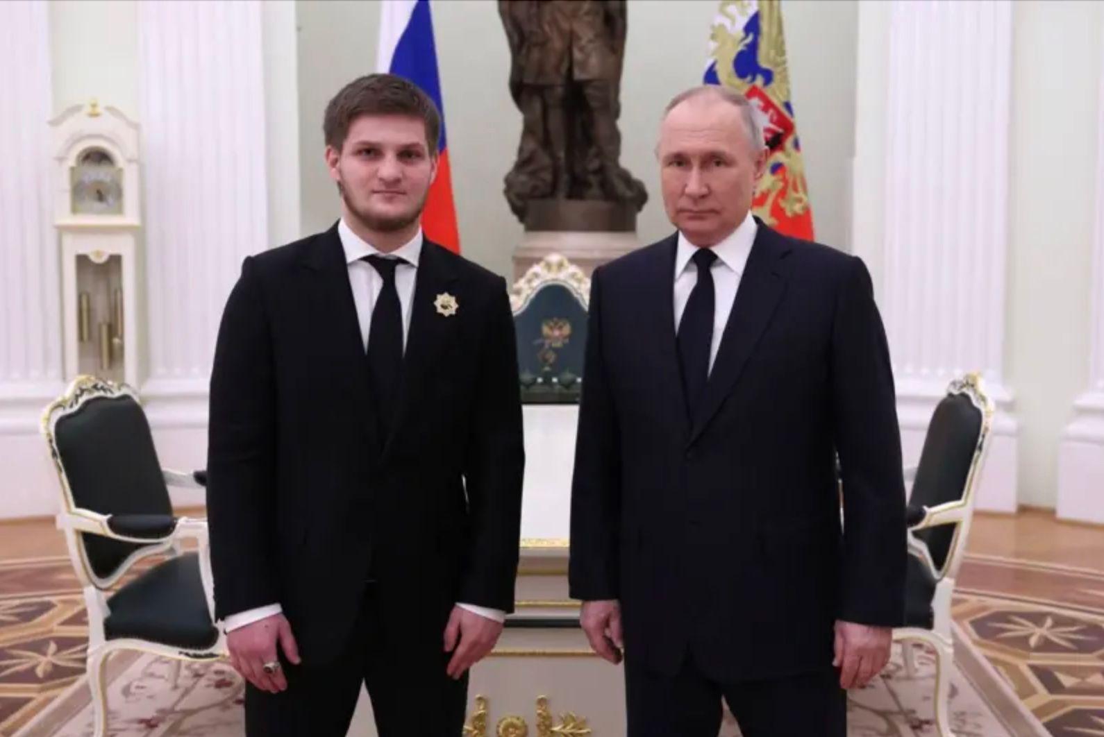 Старший син Кадирова і Володимир Путін стоять у Кремлі на тлі російських прапорів із серйозним виразом обличчя 