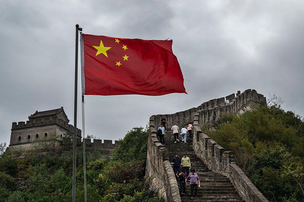 يُرى العلم الوطني على جزء من سور الصين العظيم بينما يتسلقه سياح خلال احتفالات اليوم الوطني والأسبوع الذهبي في هوايرو، على مشارف بكين. السماء ملبدة بالغيوم، الدرج الذي يتوسط السور الأثري طويل جداً، وتحيط الأشجار بطرفي السور.