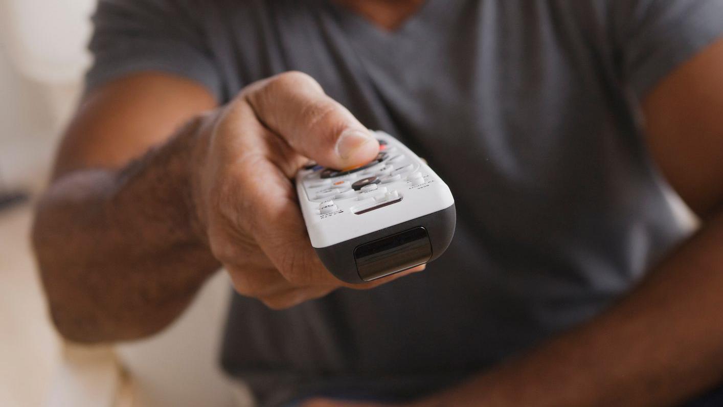 Foto de un hombre sujetando el control remoto de un televisor