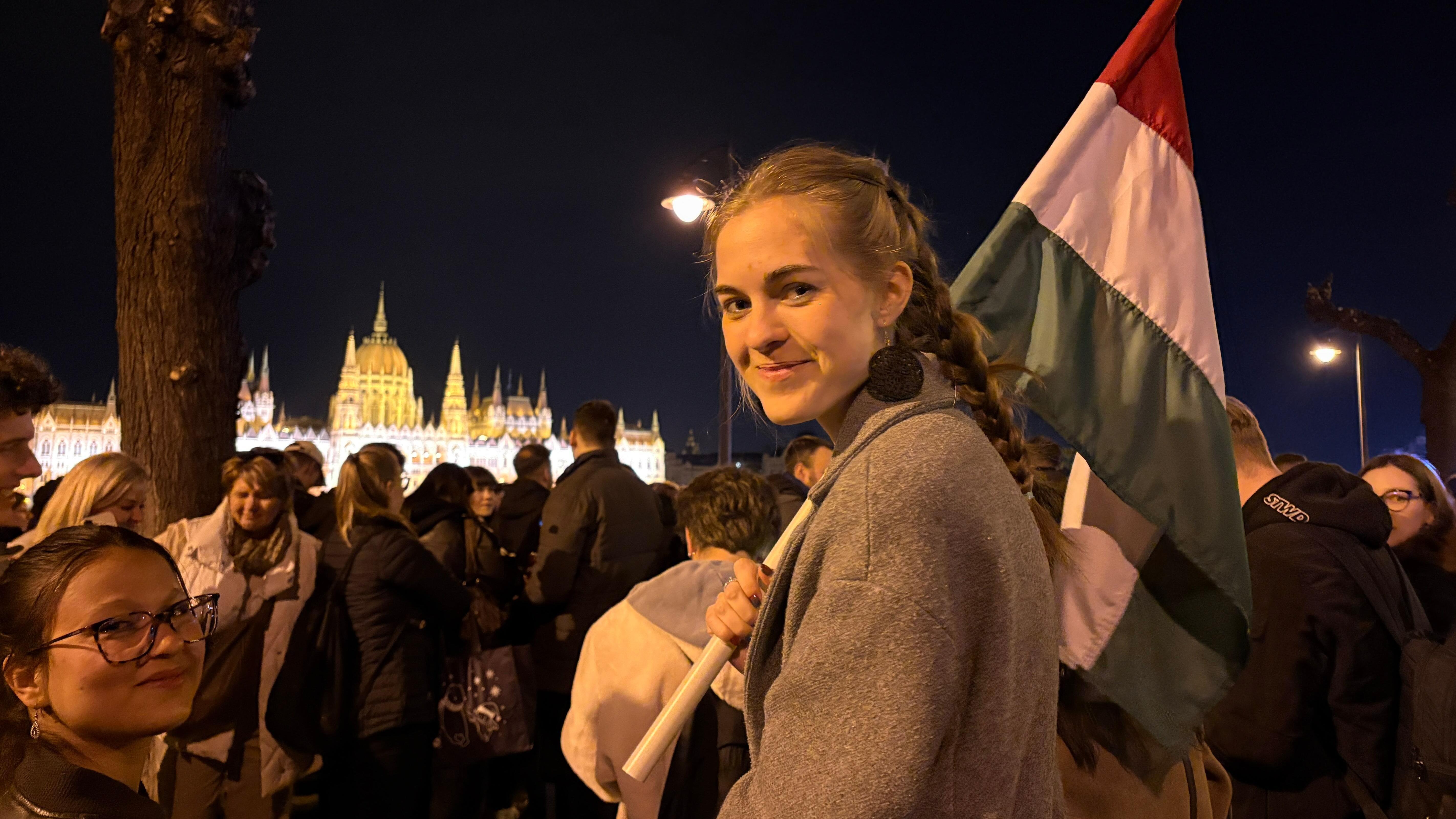 Una joven con el pelo largo trenzado sostiene una bandera de Hungría durante las celebraciones frente al parlamento nacional, a orillas del río Danubio.