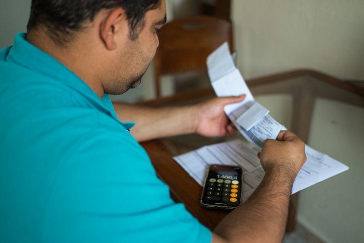Homem diante da mesa com papéis, boletos e calculadora