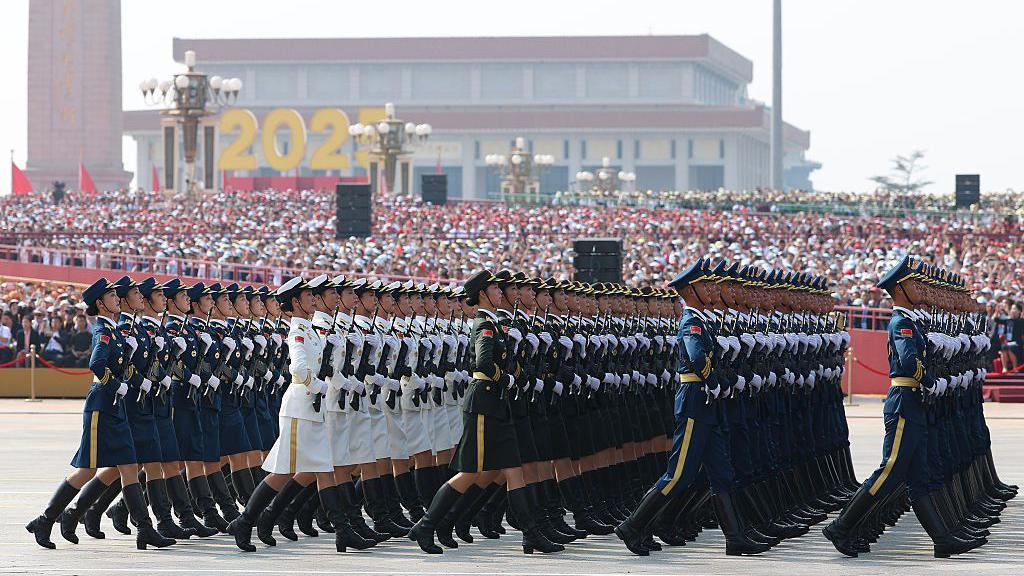 Soldados em uniformes cerimoniais marcham em frente a um pódio lotado