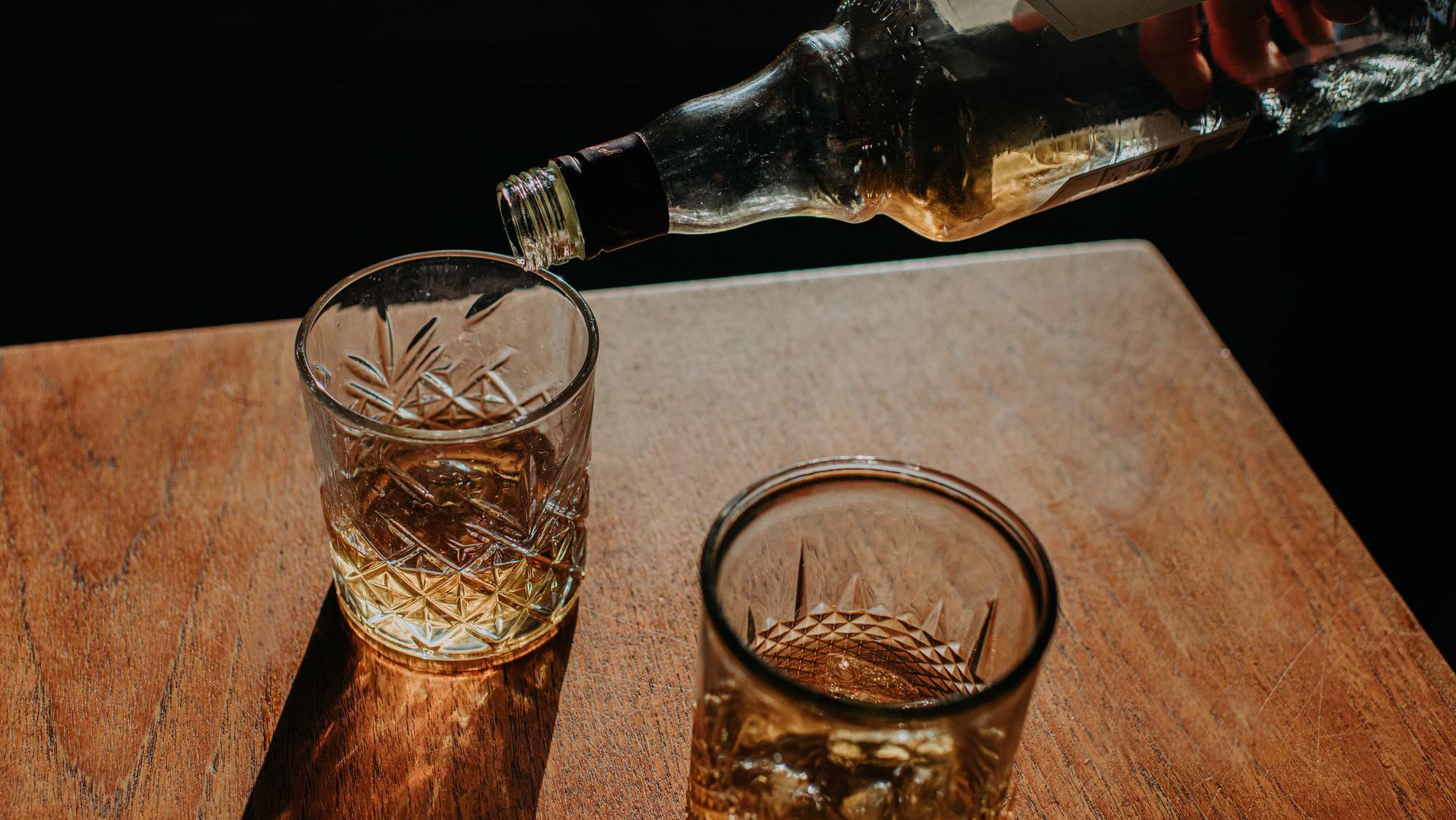 Dois copos de bebida sendo servidos por uma pessoa segurando uma garrafa. 