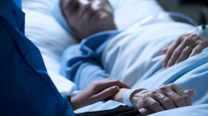 Pessoa segurando a mão de outra, que está acamada