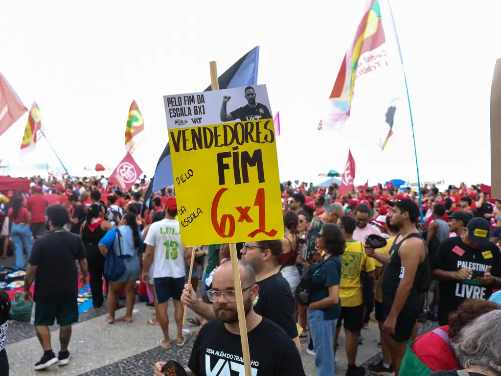 Homem segura placa pelo fim da escala 6x1 em ato do 1&ordm; de maio no Rio de Janeiro na praia de Copacabana