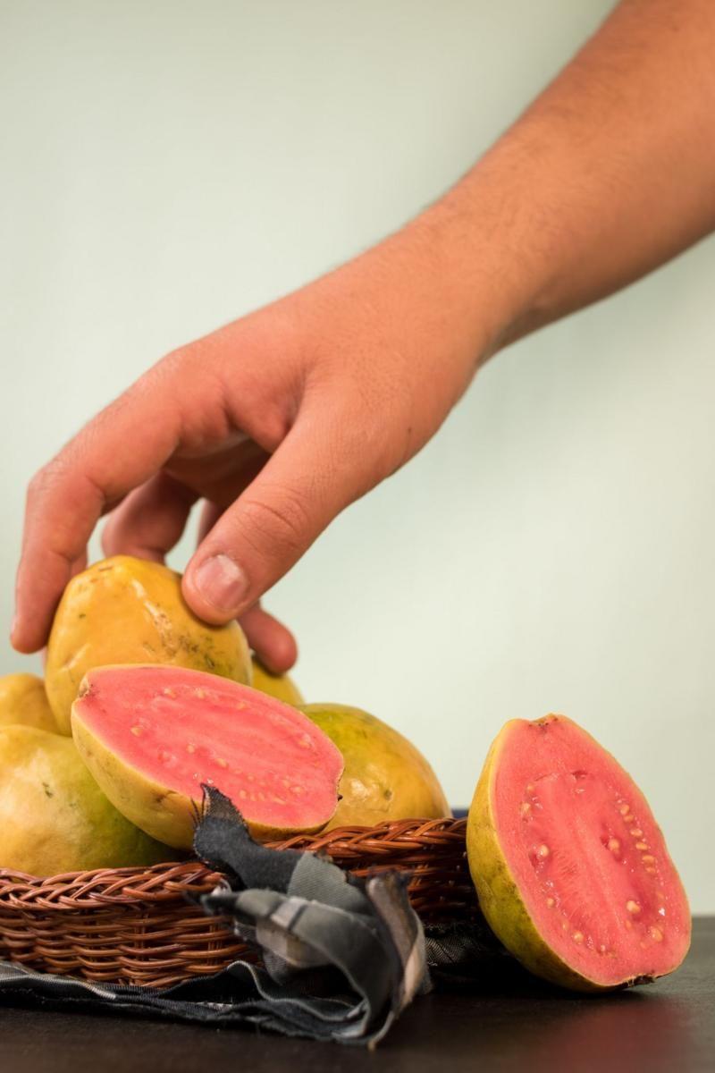 Mão pega uma goiaba de um cesto das frutas sobre uma mesa