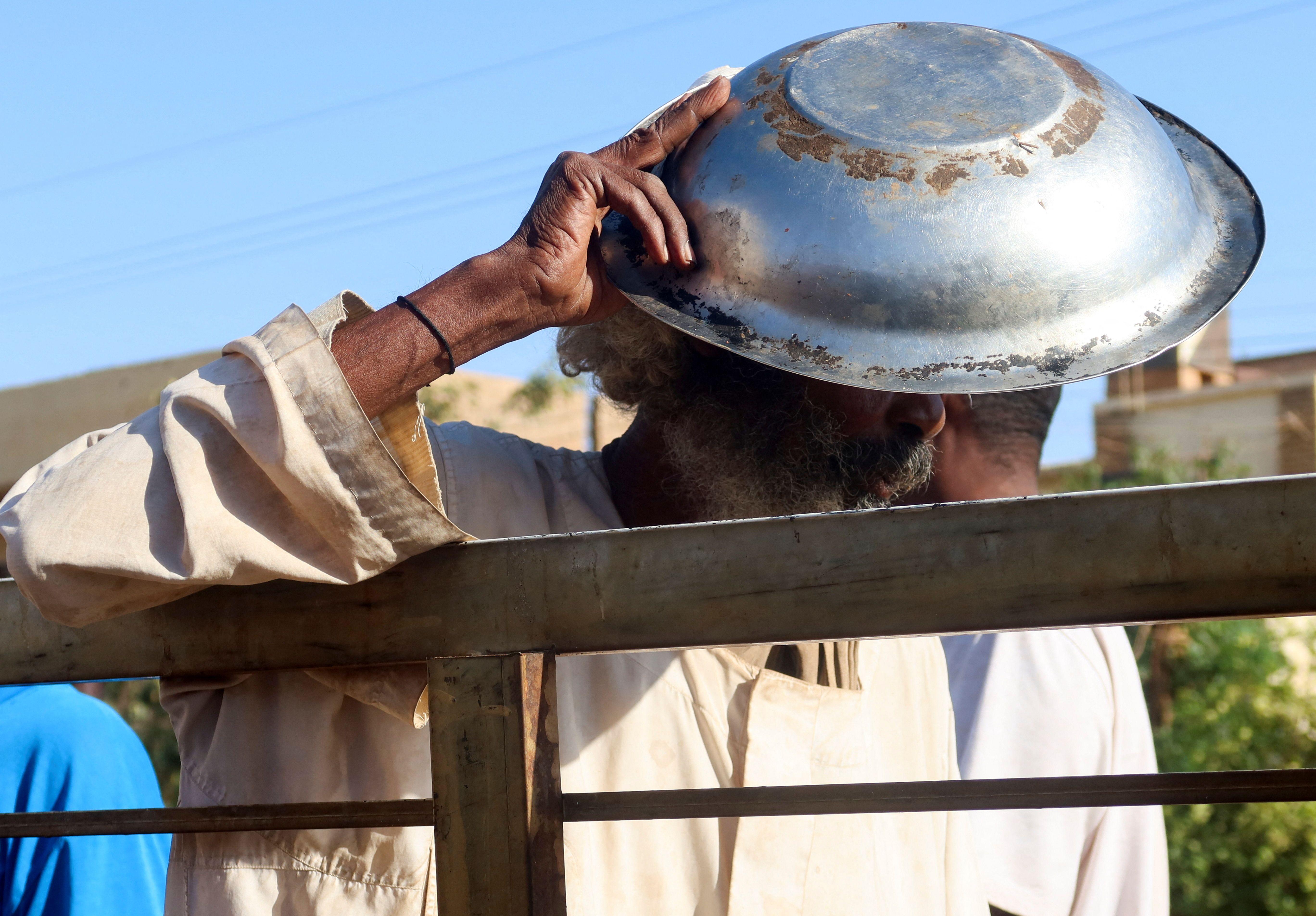 رجل سوداني يحتمي من الشمس بقدر طعام بينما ينتظر في طابور للحصول على حصة غذائية في أم درمان
