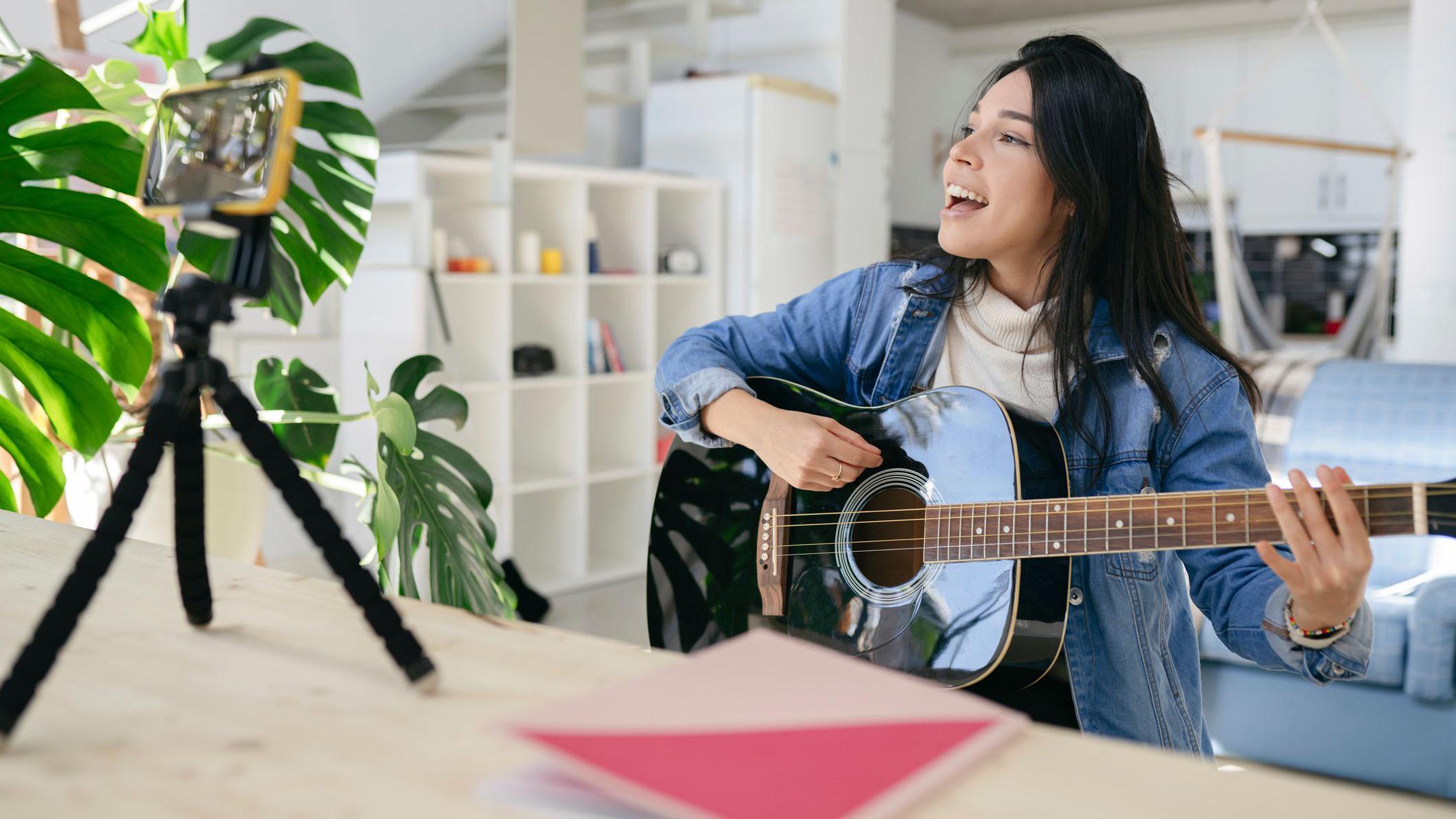 فتاة تثبّت هاتفها على قاعدة أمامها، تعزف وتغنّي
