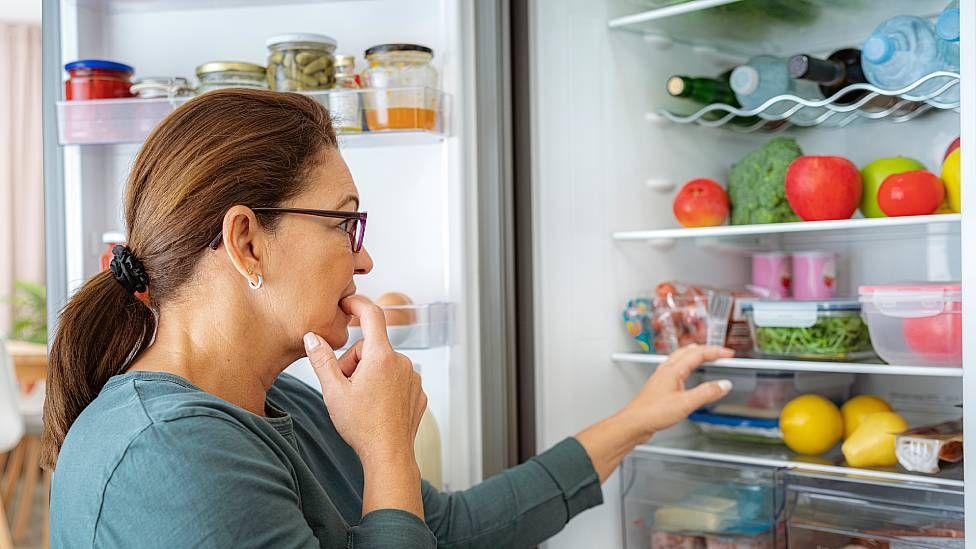 Mujer mirando al interior de la nevera mientras elige un alimento
