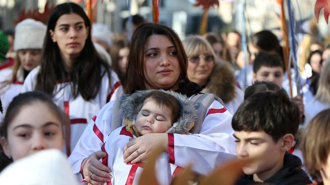 Žena u naručju drži dečaka koji spava u tradicionalnoj gruzijskoj odeći