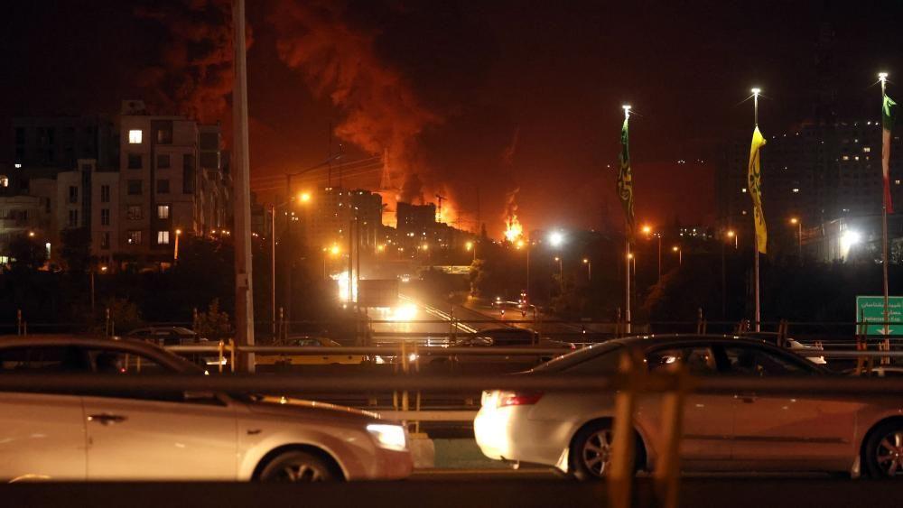 Autos en las calles de Teherán mientras el fuego y el humo se elevan desde un almacén de petróleo el 15 de junio de 2024.
