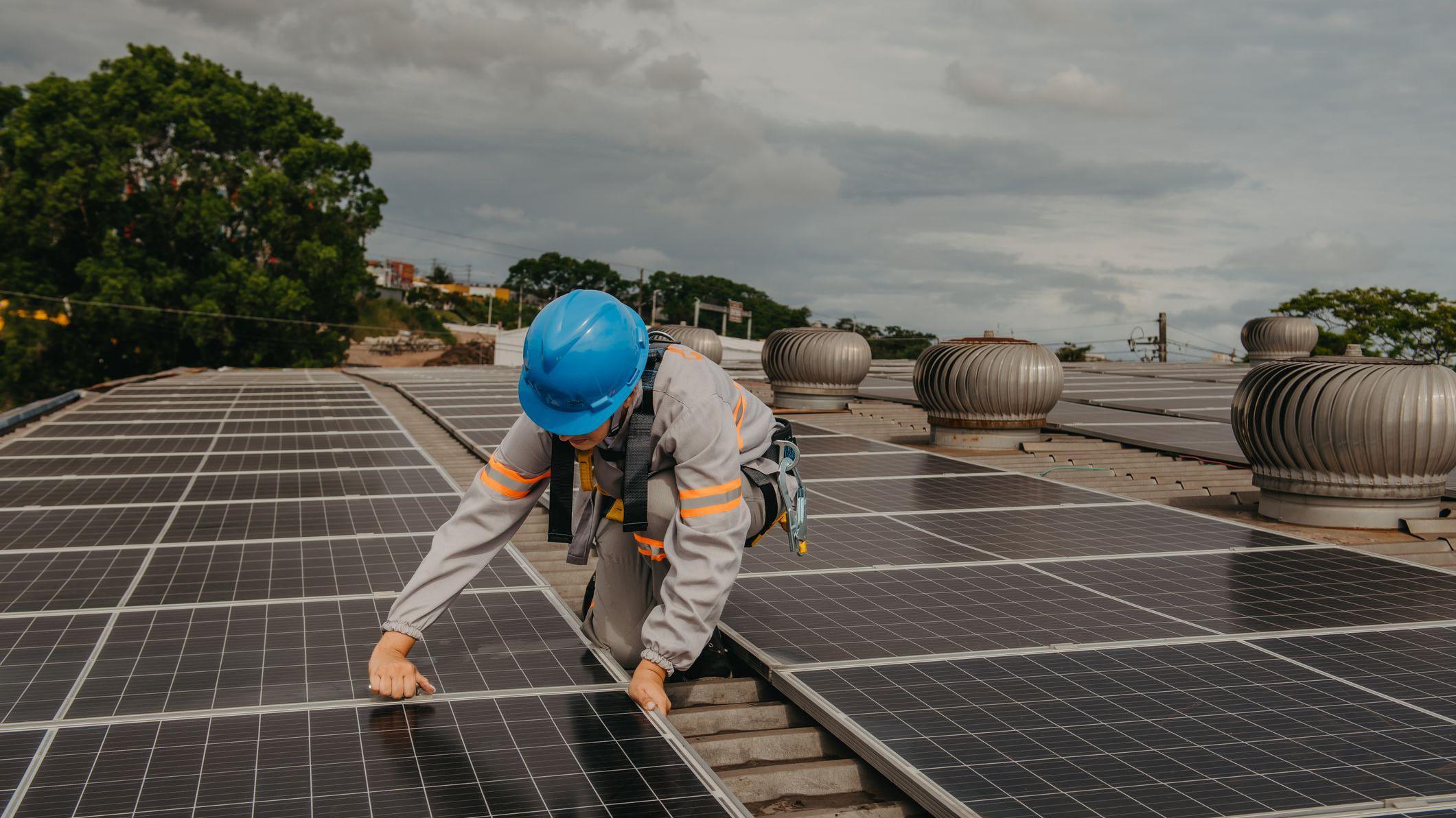 Mulher de uniforme e capacete trabalhando na instalação de painéis solares
