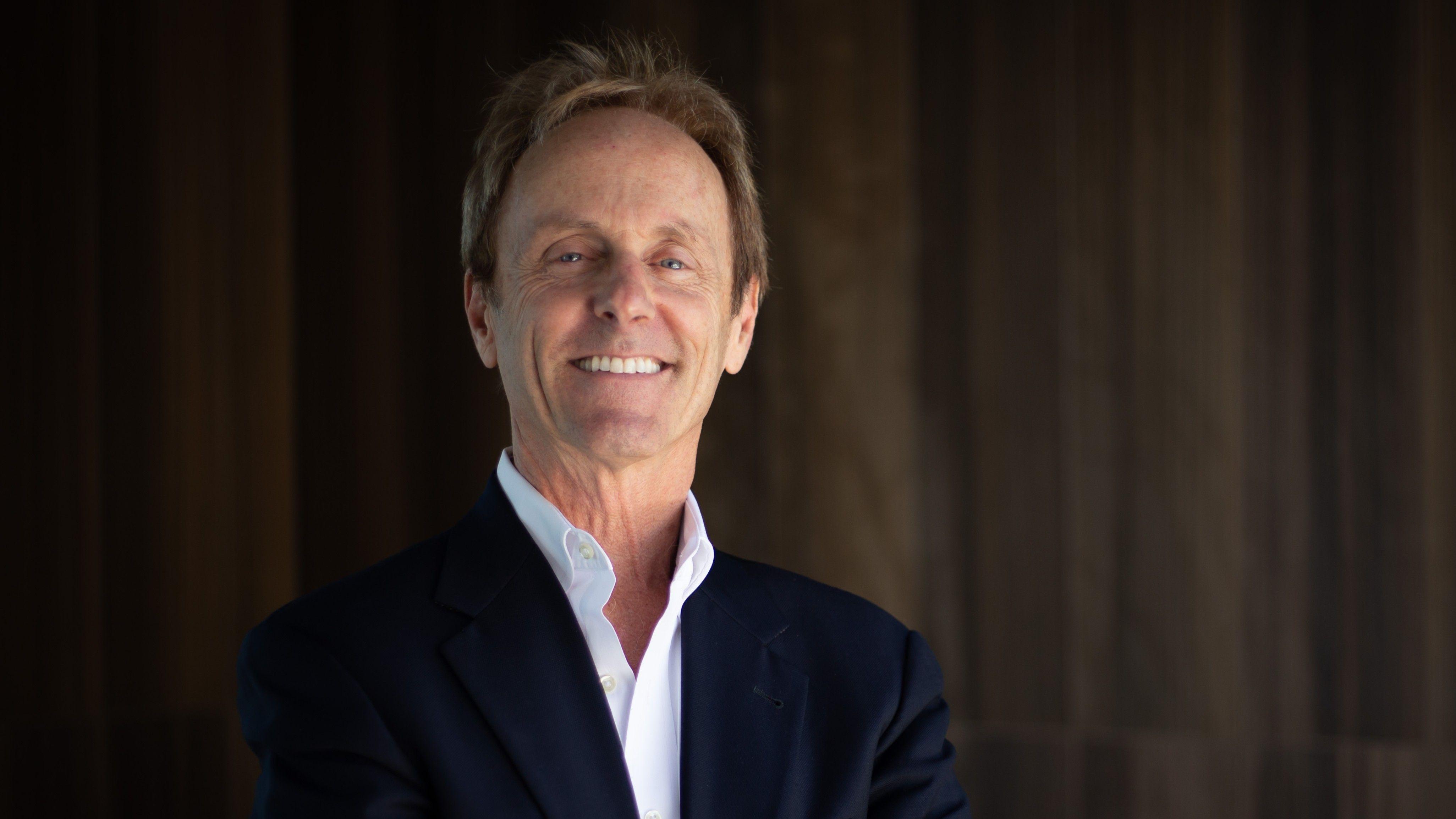 조쉬 버신은 어두운 색 재킷 안에 흰색 셔츠를 입고 있다