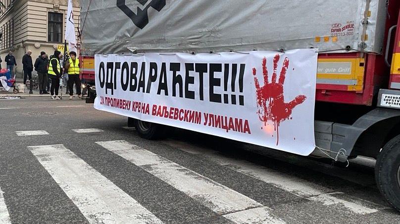 Na belom transparentu prikačenom za kamion ispisano je 'Odgovaraćete za prolivenu krv na valjevskim ulicama sa crvenom šakom'