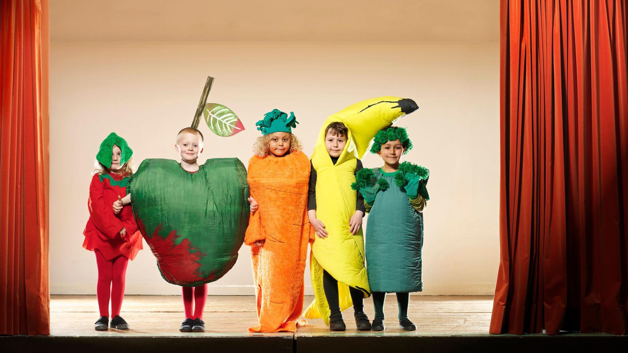 أطفال يقفون على مسرح، ويلعبون أدواراً تمثّل كل منها فاكهة معينة.