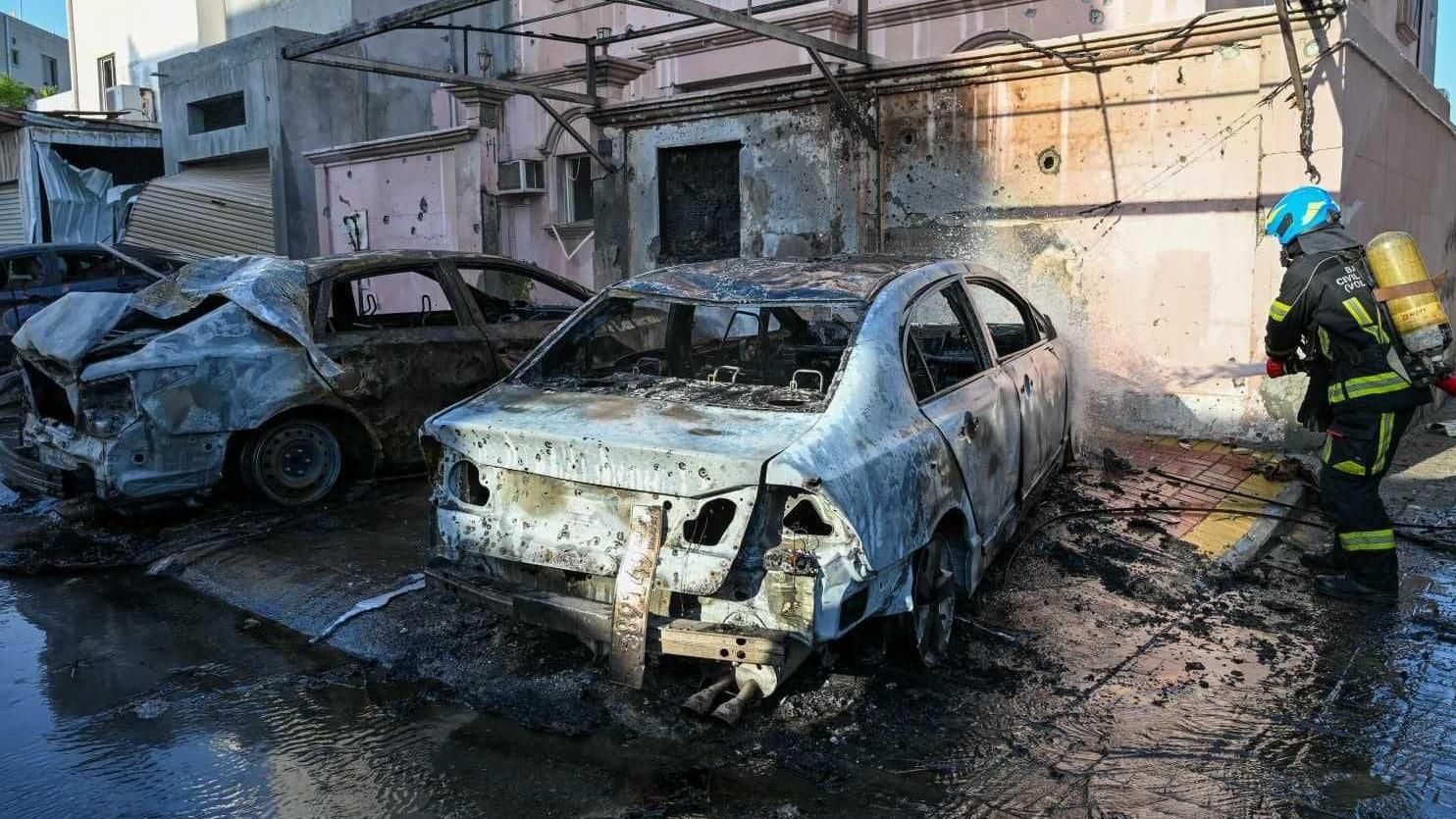 Un bombero echa agua con una manguera en dirección de unos autos quemados por la caída de esquirlas de drones
