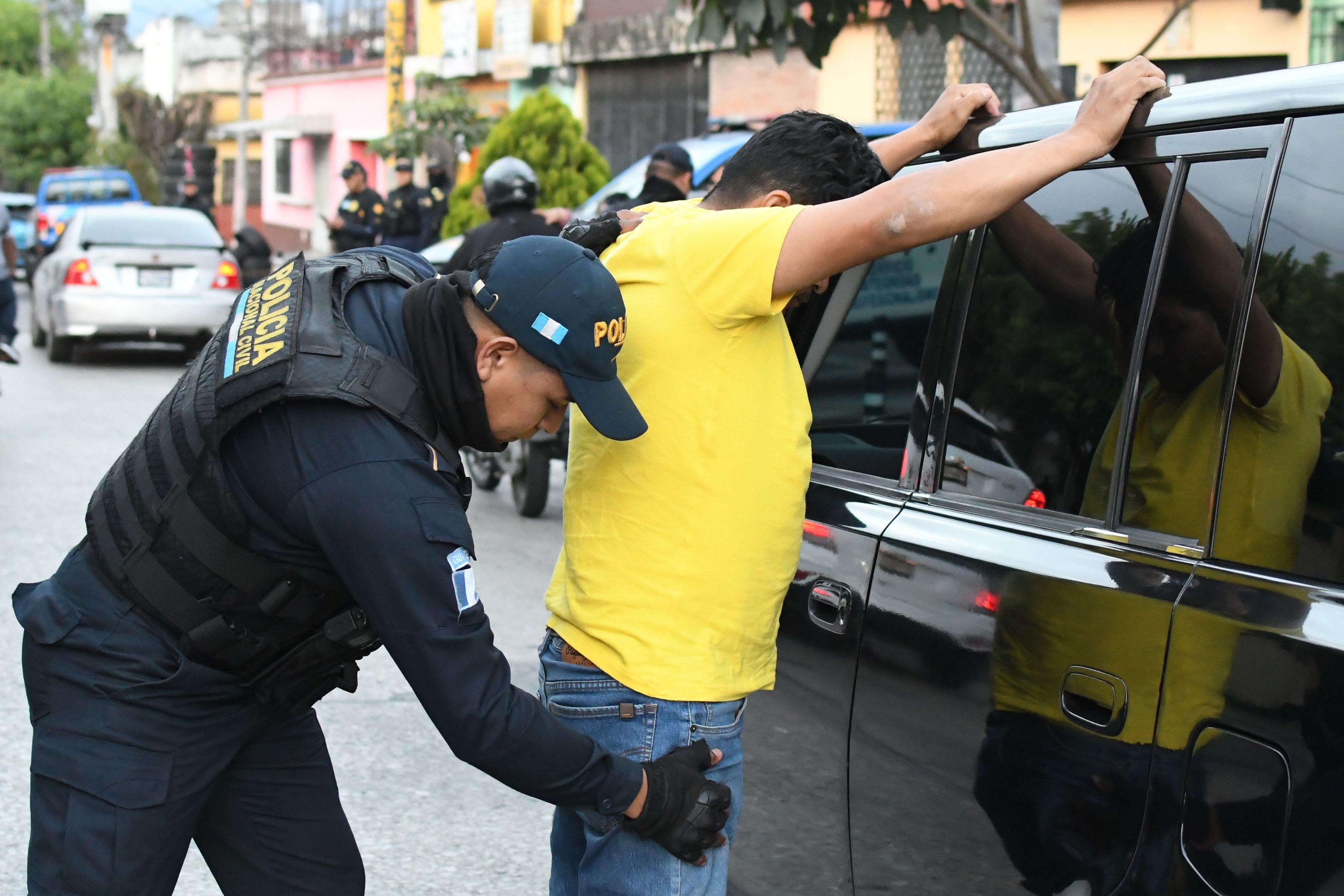 Un policía cachea a un hombre junto a un auto. 