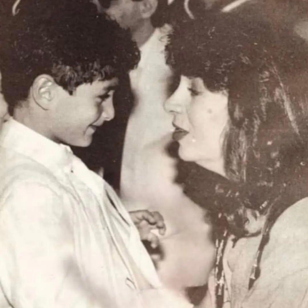 الفنانة سمية الألفي تنظر وتبتسم لنجلها أحمد الفيشاوي عندما كان طفلاً، بينما ينظر هو إليها ويبادلها أيضاً ابتسامة.