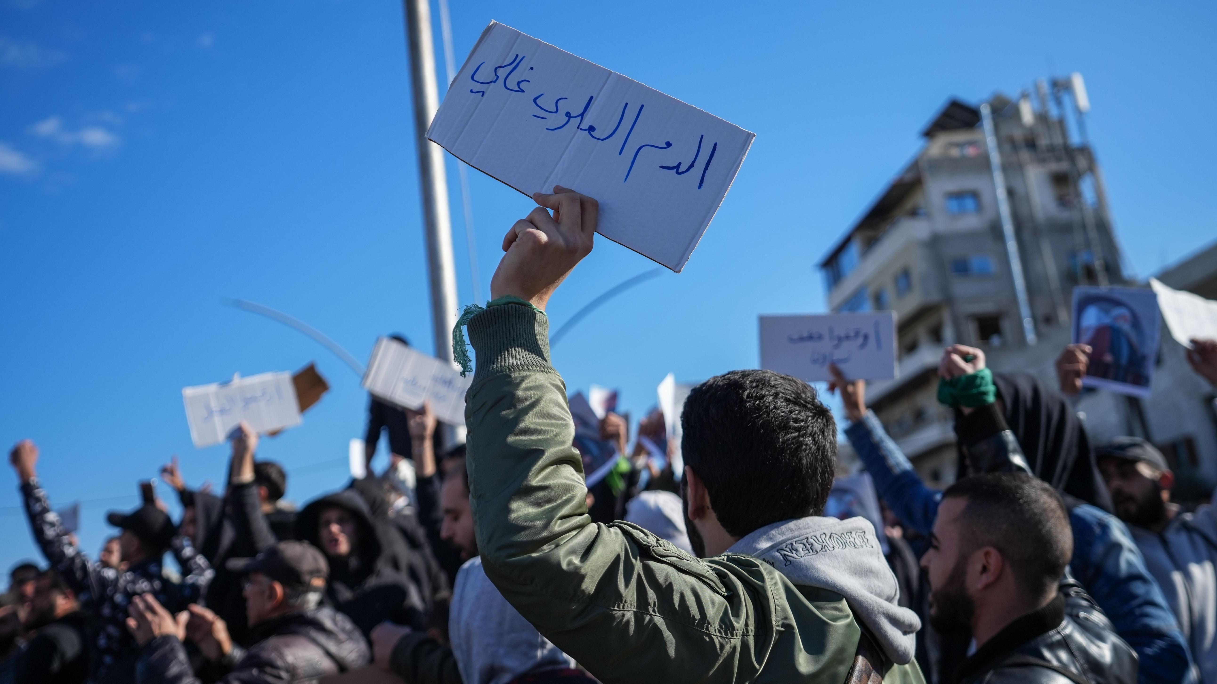 يرفع أحد المتظاهرين لافتة كُتب عليها باللغة العربية "دم العلويين ثمين" بينما تجمع أفراد من الطائفة العلوية للاحتجاج على العنف الممارس ضد العلويين في أعقاب تفجير مسجد حمص، في مدينة اللاذقية بسوريا، في 28 ديسمبر/ كانون الأول 2025.