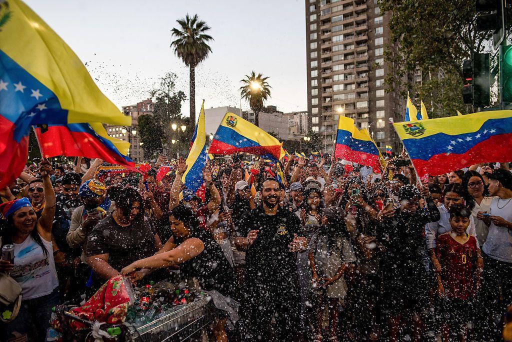 Un montónd de gente agrupada, ondenado banderas venezolanas y en un claro ambiente festivo en Santiago de Chile. 