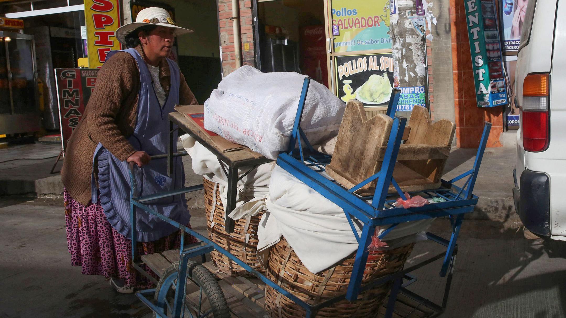 Una mujer empuja un carro con enseres y cestos de mimbre en una calle de Bolivia