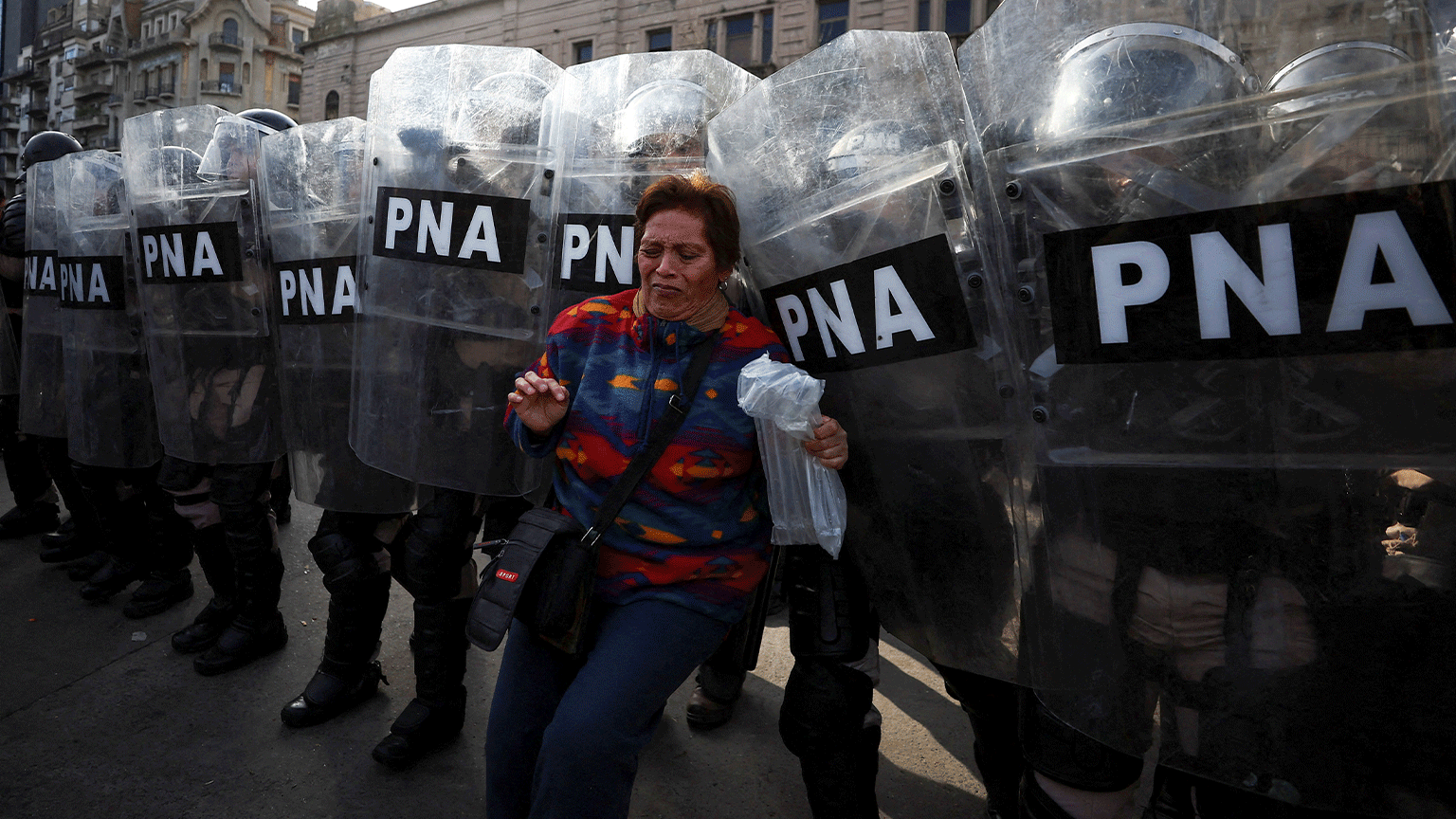 Uma mulher na frente de vários policiais com escudos