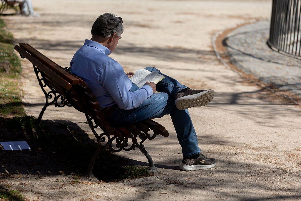 
Um homem sentado no banco de uma pra&ccedil;a lendo um livro