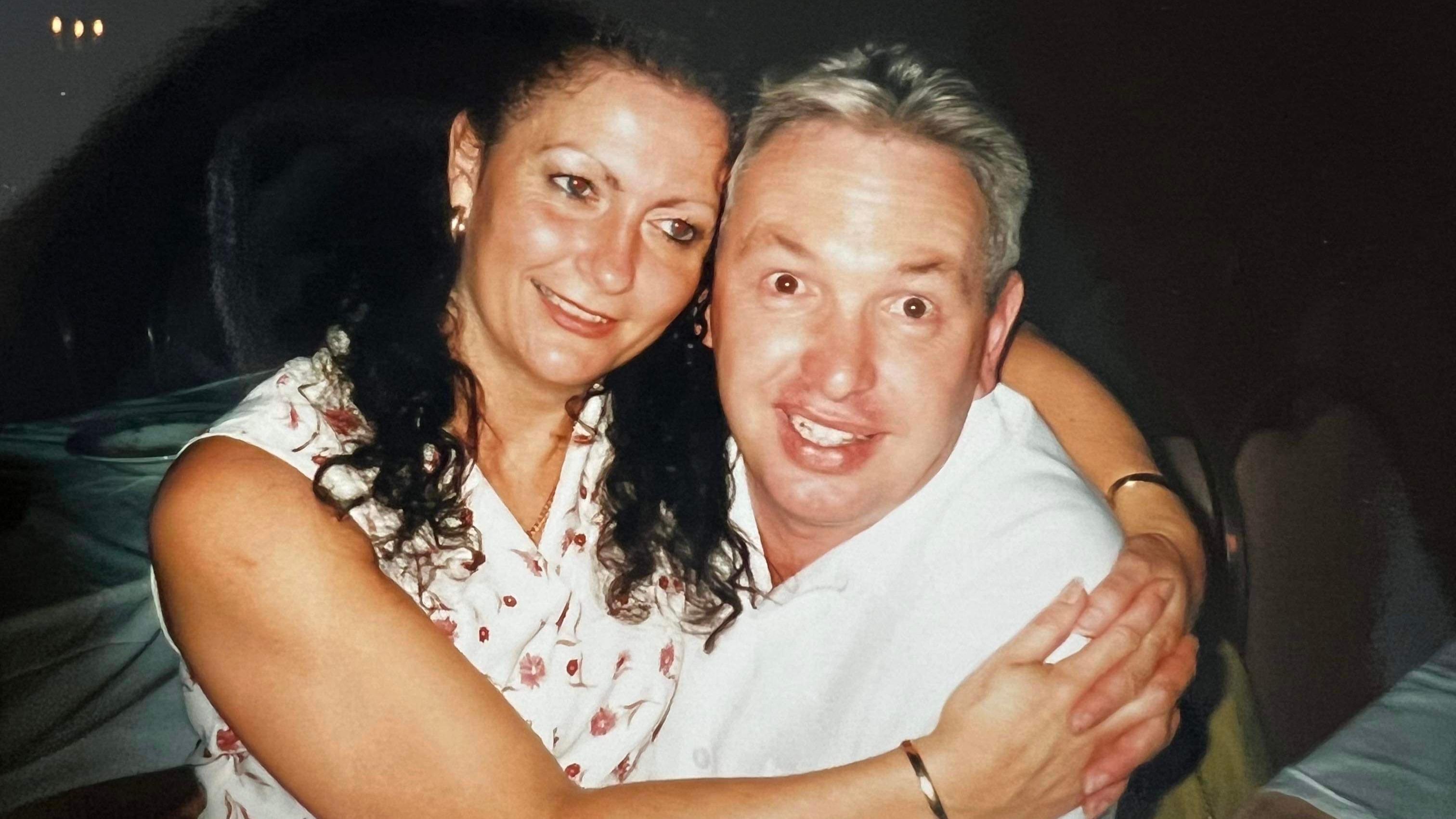  Joy, que tem longos cabelos cacheados e veste um vestido floral sem mangas, est&aacute; nos bra&ccedil;os de um homem de camisa branca.