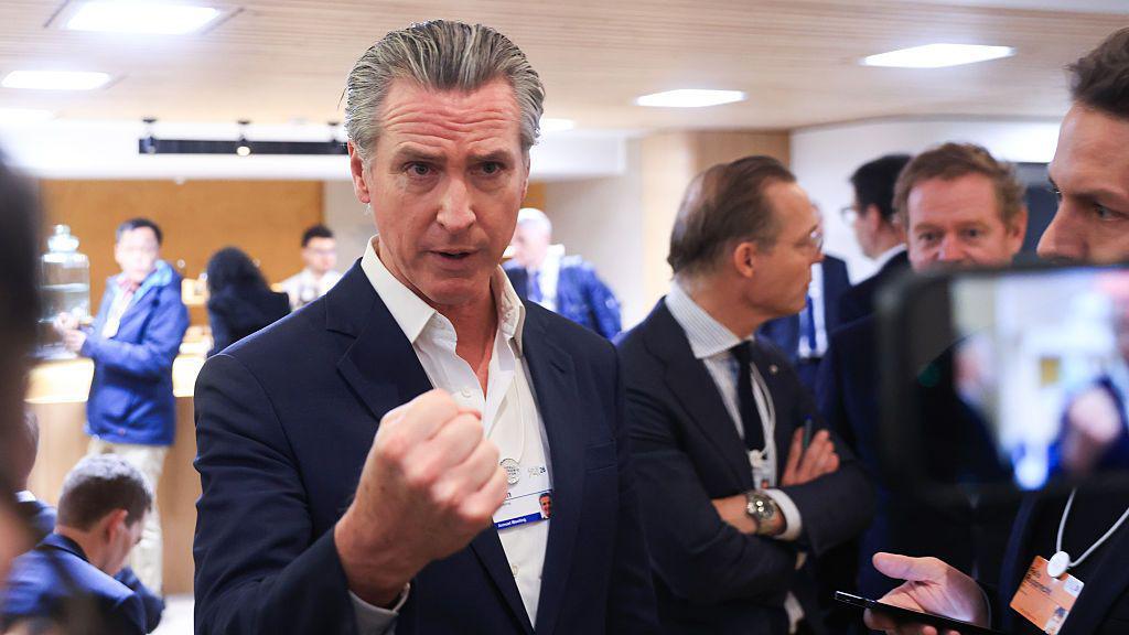 El gobernador Gavin Newsom habla ante reporteros en un salón de DAvos