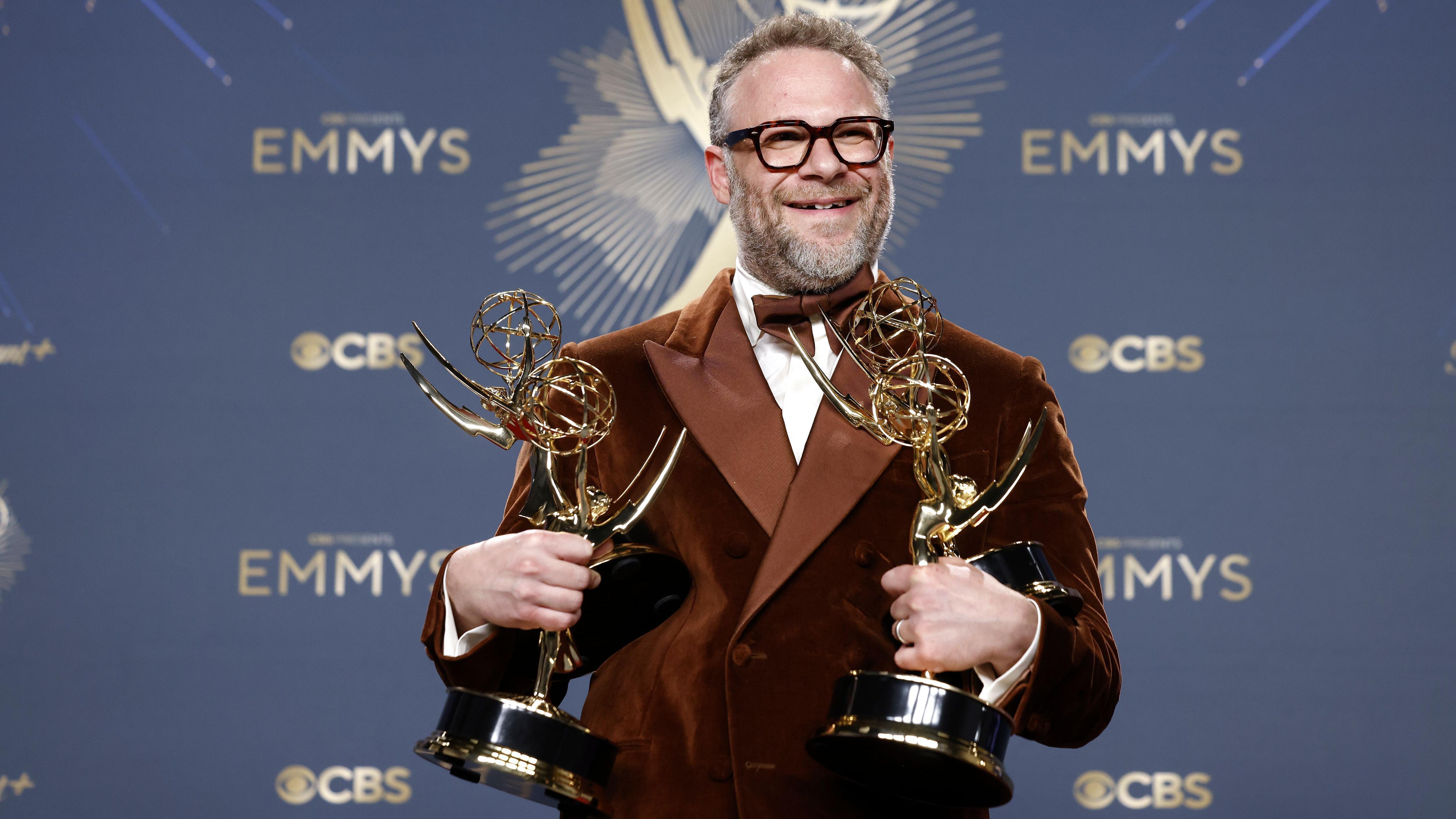Seth Rogen vestido con un traje burgundy, camisa blanca y pajarita, posa con los cuatro premios Emmy obtenidos por la serie cómica El estudio.