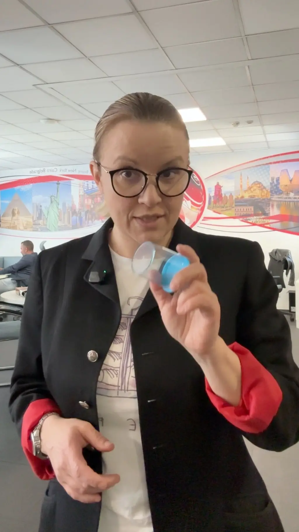 Novinarka drži čašicu za testiranje urina u ruci i objašnjava šta boja urina govori o zdravlju.