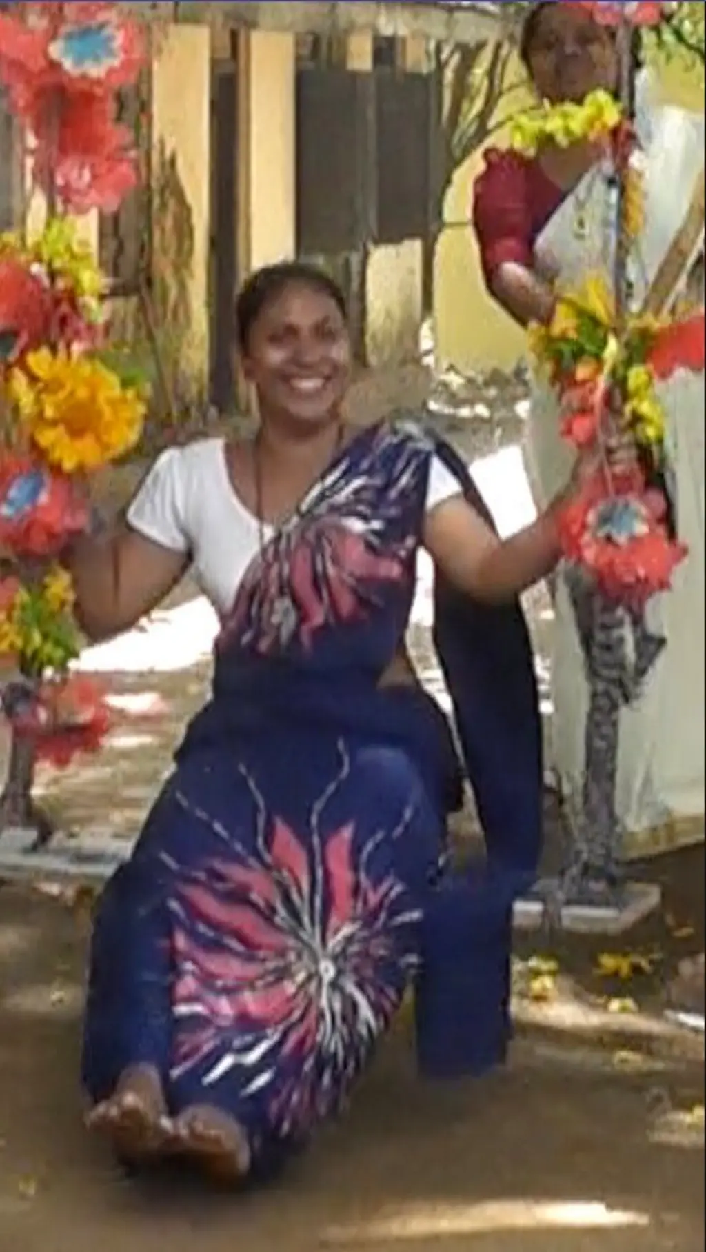 නිල් පැහැති සාරියක් ඇඳ සිටින තරුණියක් සිනහ මුසු මුහුණින් ඔන්චිලාවක සිටින අතර එහි ලනු මල් වලින් සරසා තිබේ.