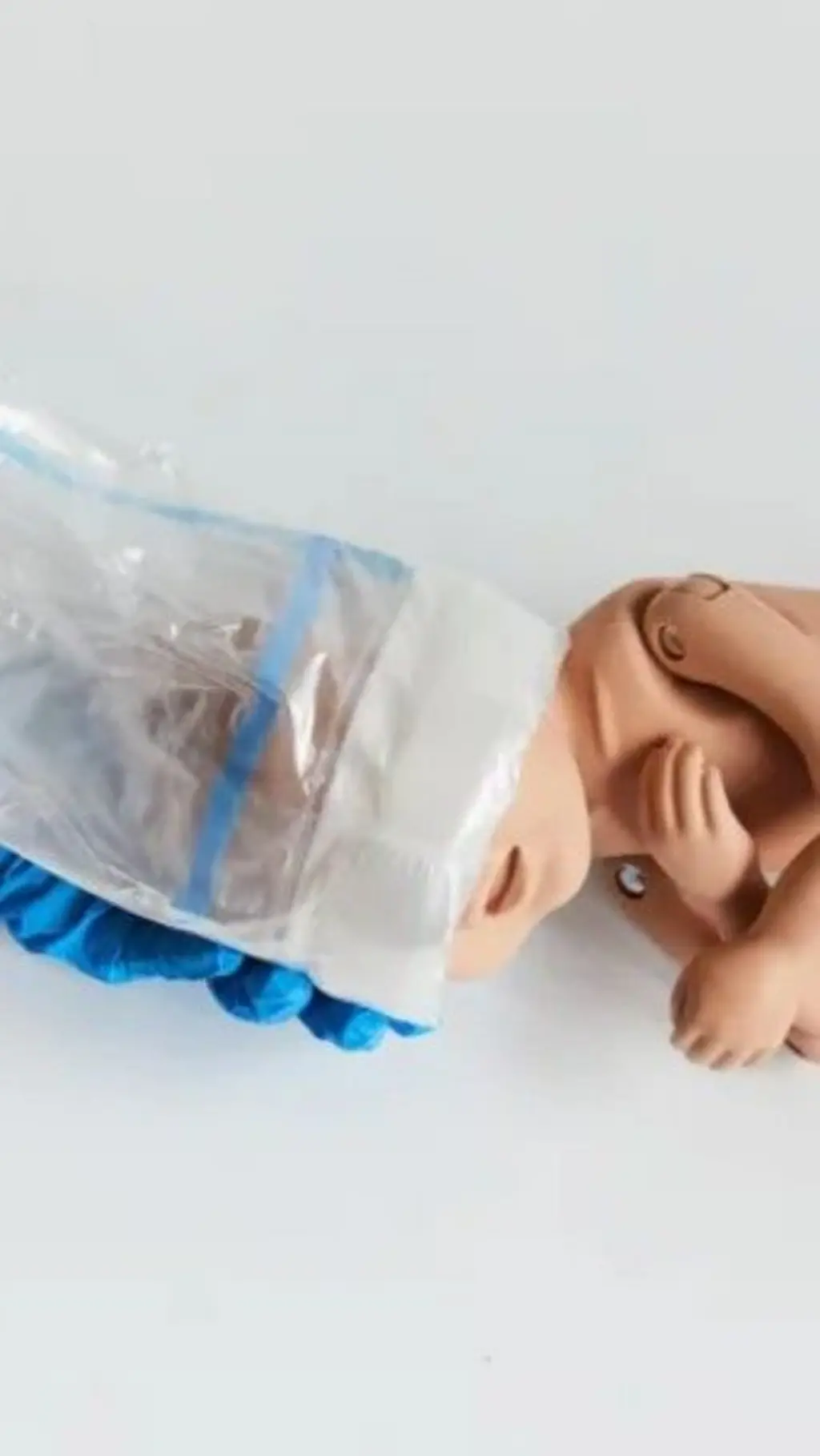 Bebê de brinquedo com uma espécie de sacola ao redor da cabeça
