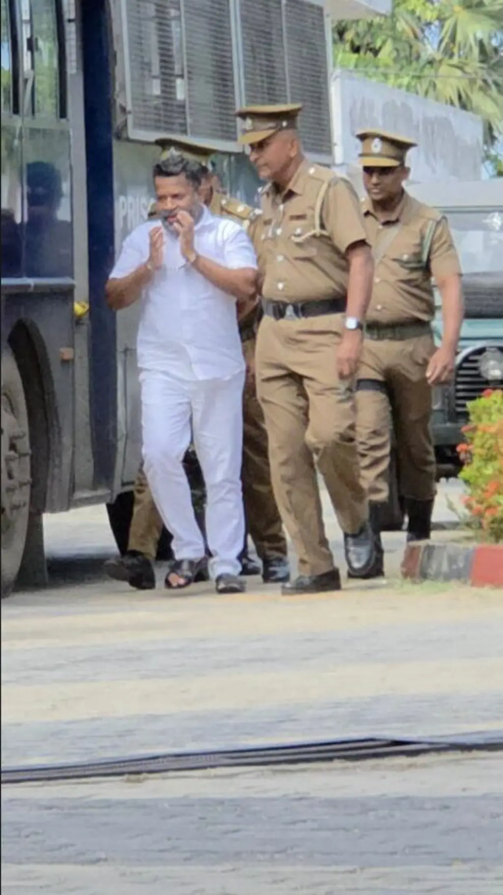 සුදුපාට ඇඳුමක් ඇඳගත් පුද්ගලයෙකු මාංචු දම බන්ධනාගාර නිලධාරීන් රැගෙන යයි.