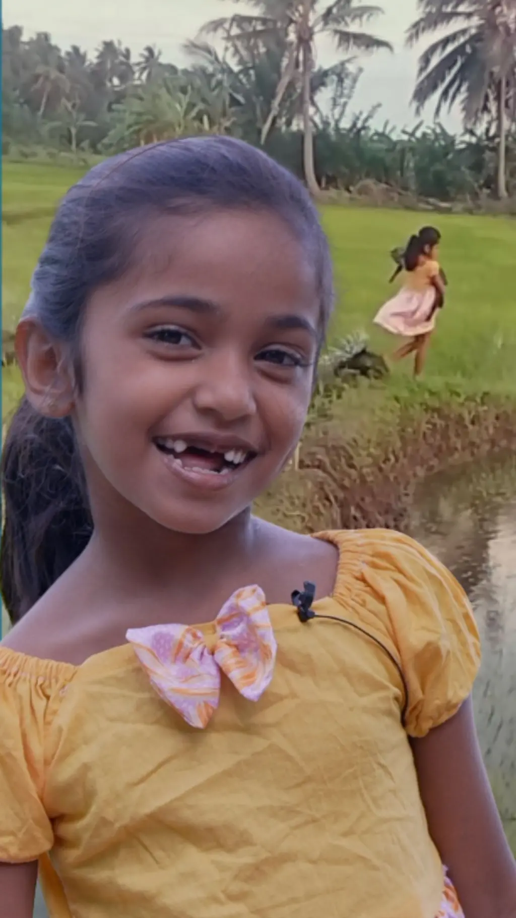 දැරියක් කුඹුරු යායක් මැදින් දුවන අතර ඇගේ මුහුණ විශාල ෆොටෝ එකක් ද පෙනේ.