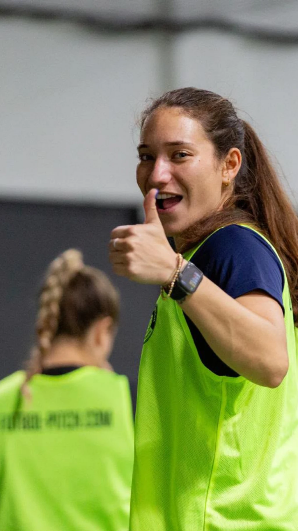 Mujer joven mirando a la cámara, sonriendo y levantando el pulgar de la mano izquierda.